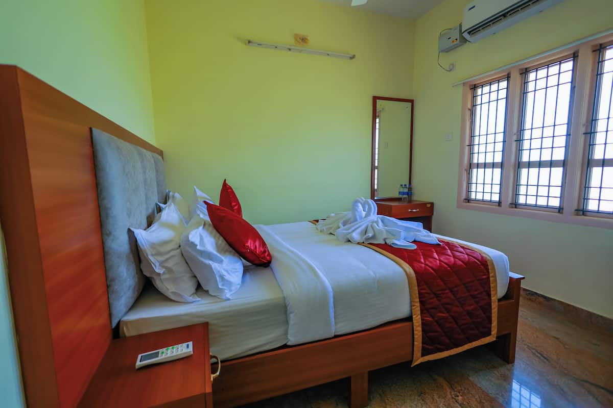 A neatly made bed with white and red bedding, a bedside table with a remote control, and a window with bars.