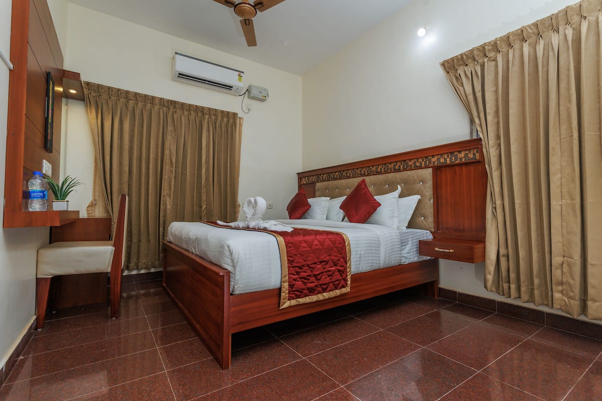 A hotel room with a wooden bed, a desk, a chair, an air conditioning unit, and curtains.