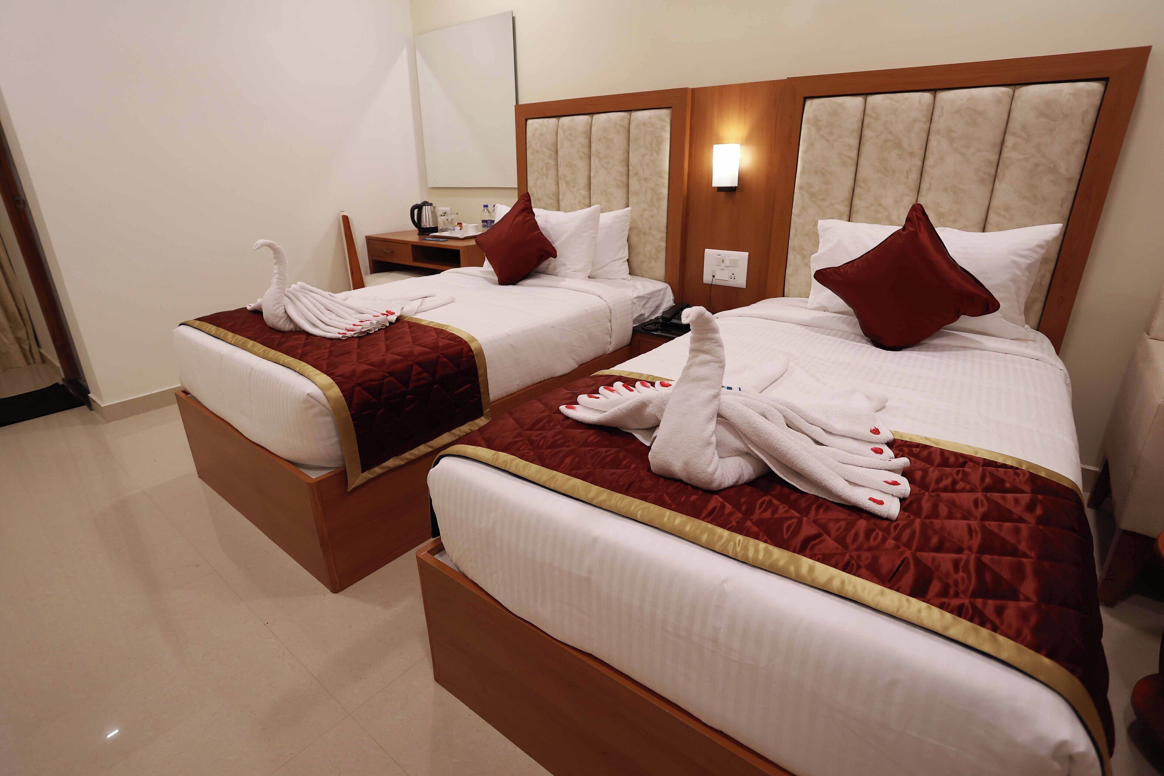 Habitación de hotel con dos camas, cada una con una colcha roja y blanca, y un cabecero de madera.