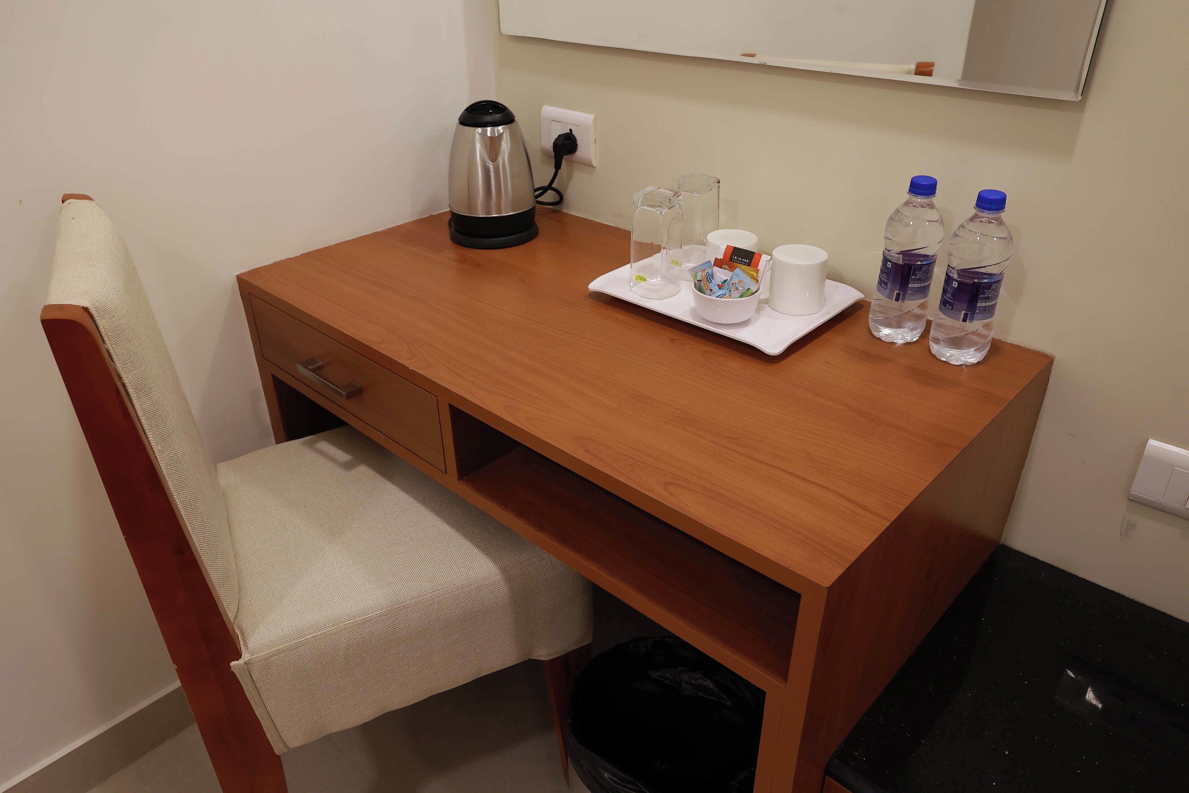 A wooden desk with a kettle, two water bottles, a cup, and a tray with a tissue box.
