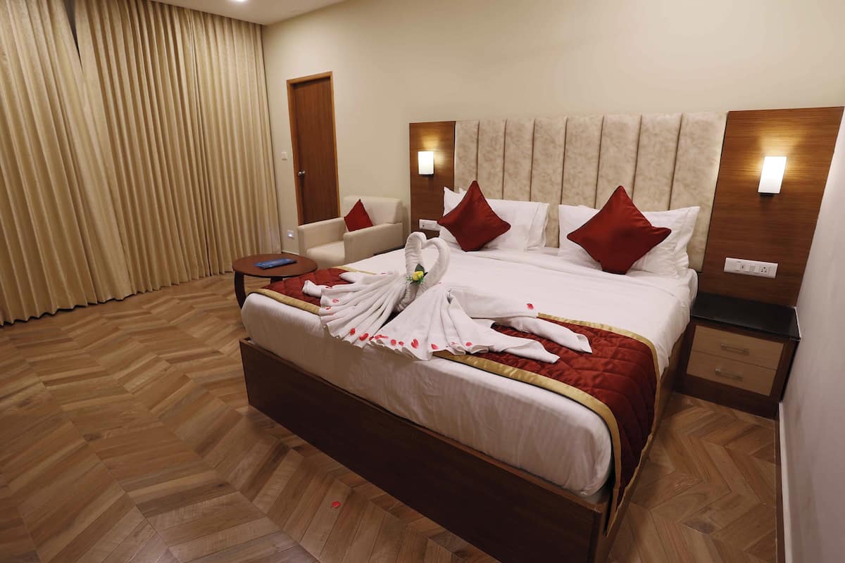 A hotel room with a large bed, a bedside table, a chair, a wooden floor, and a curtain.