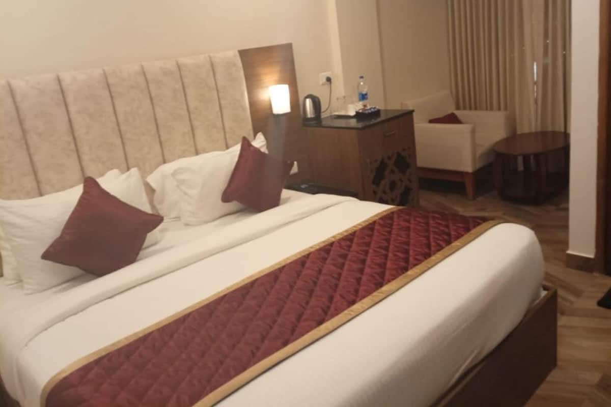 A hotel room with a large bed, a bedside table with a lamp, a chair, and a small round table.