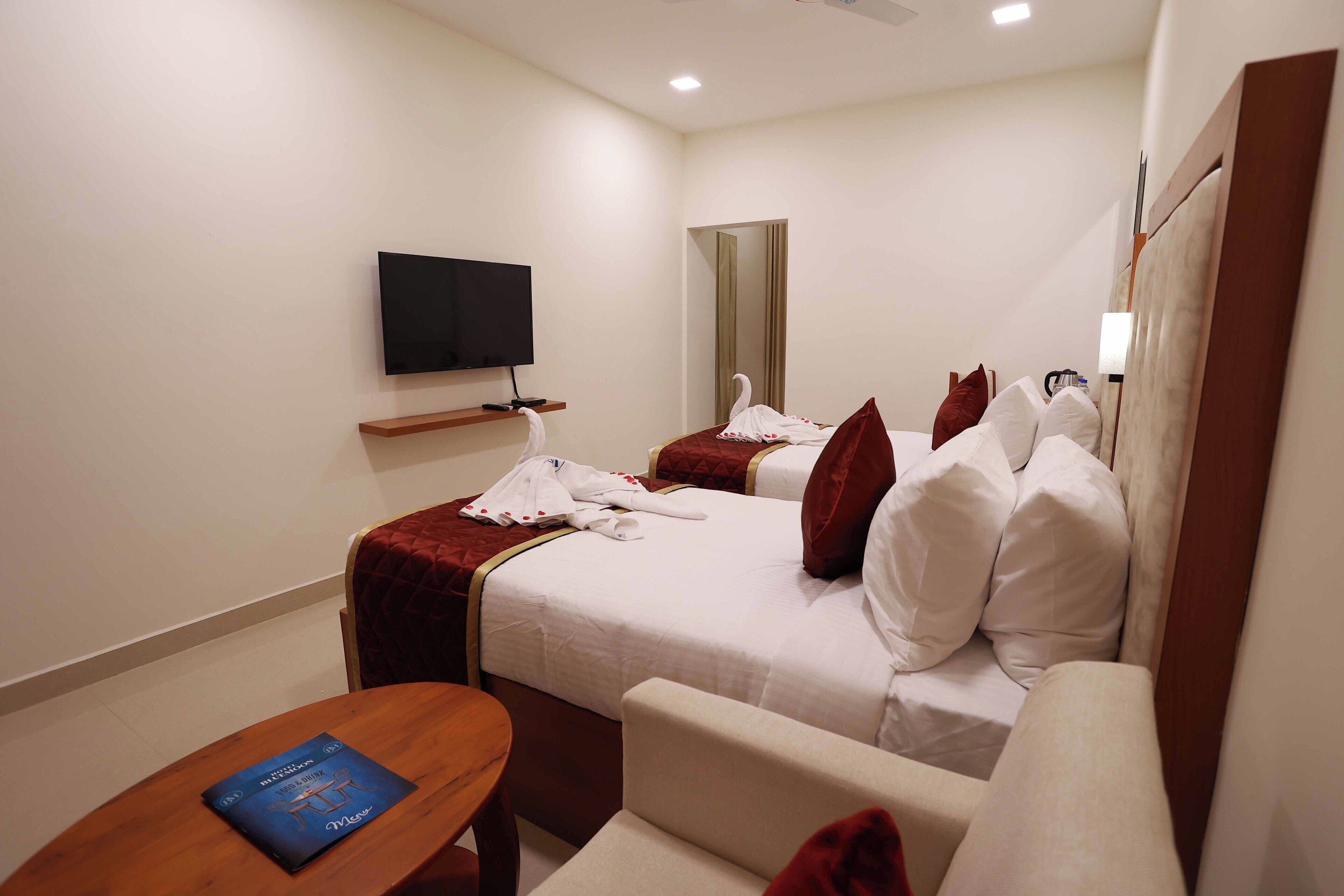Una habitación de hotel con dos camas, un televisor, un espejo y una mesita con un libro.