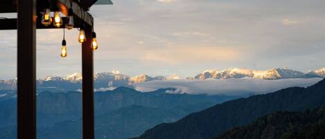 A mountainous landscape with a wooden pergola and hanging light bulbs.
