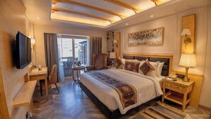 A hotel room with a large bed, a desk, a chair, a TV, and a window with curtains. -  Presidium Sarovar Premiere Dalhousie (Dalhousie)