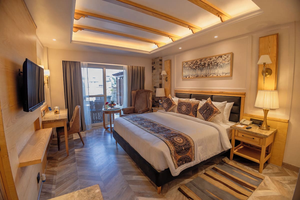 A hotel room with a large bed, a desk, a chair, a TV, and a window with curtains.