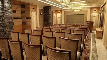 A conference room with rows of chairs, a podium, and a large screen.
