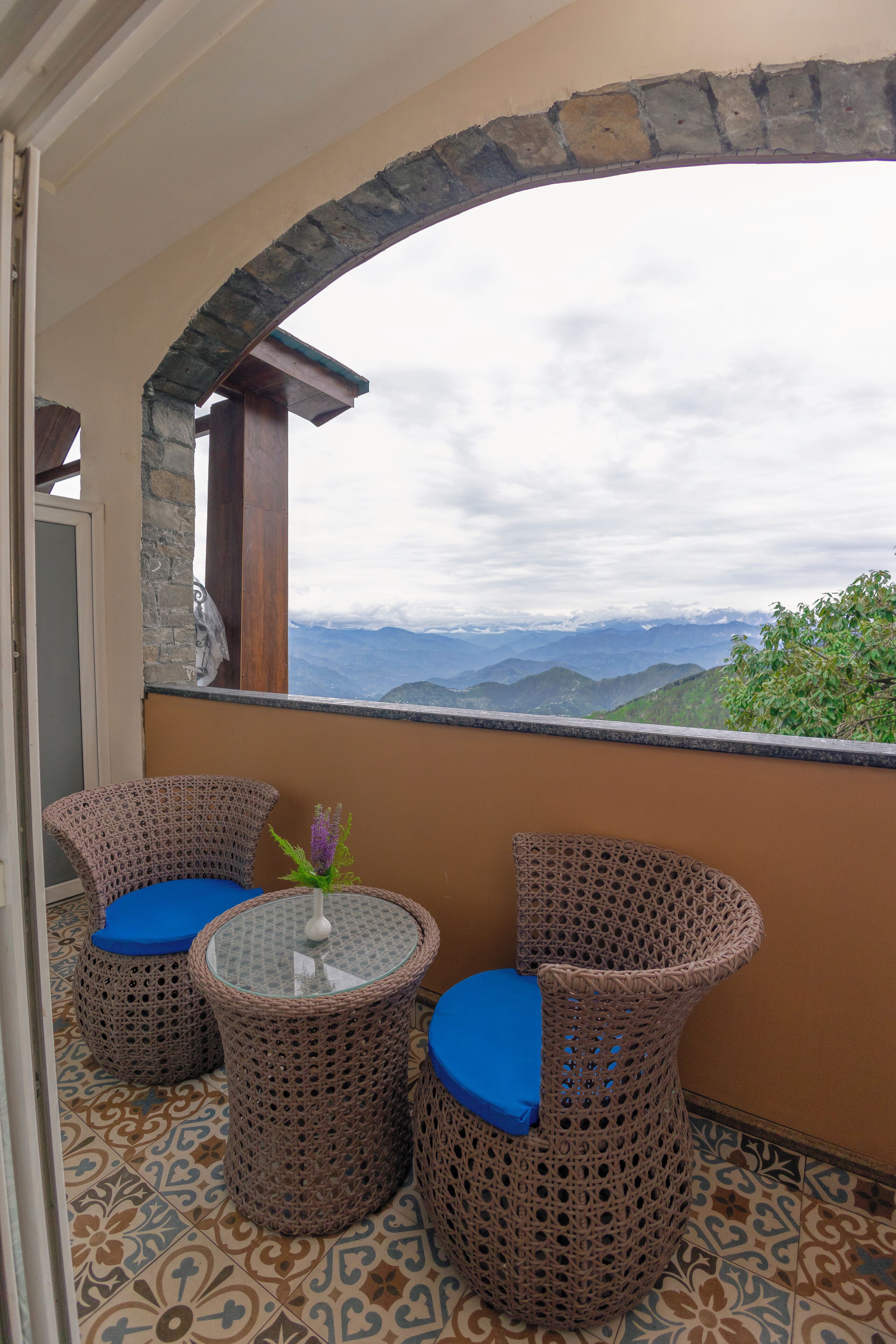 Ein Balkon mit Korbstühlen und einem kleinen Tisch, mit Blick auf eine gebirgige Landschaft.