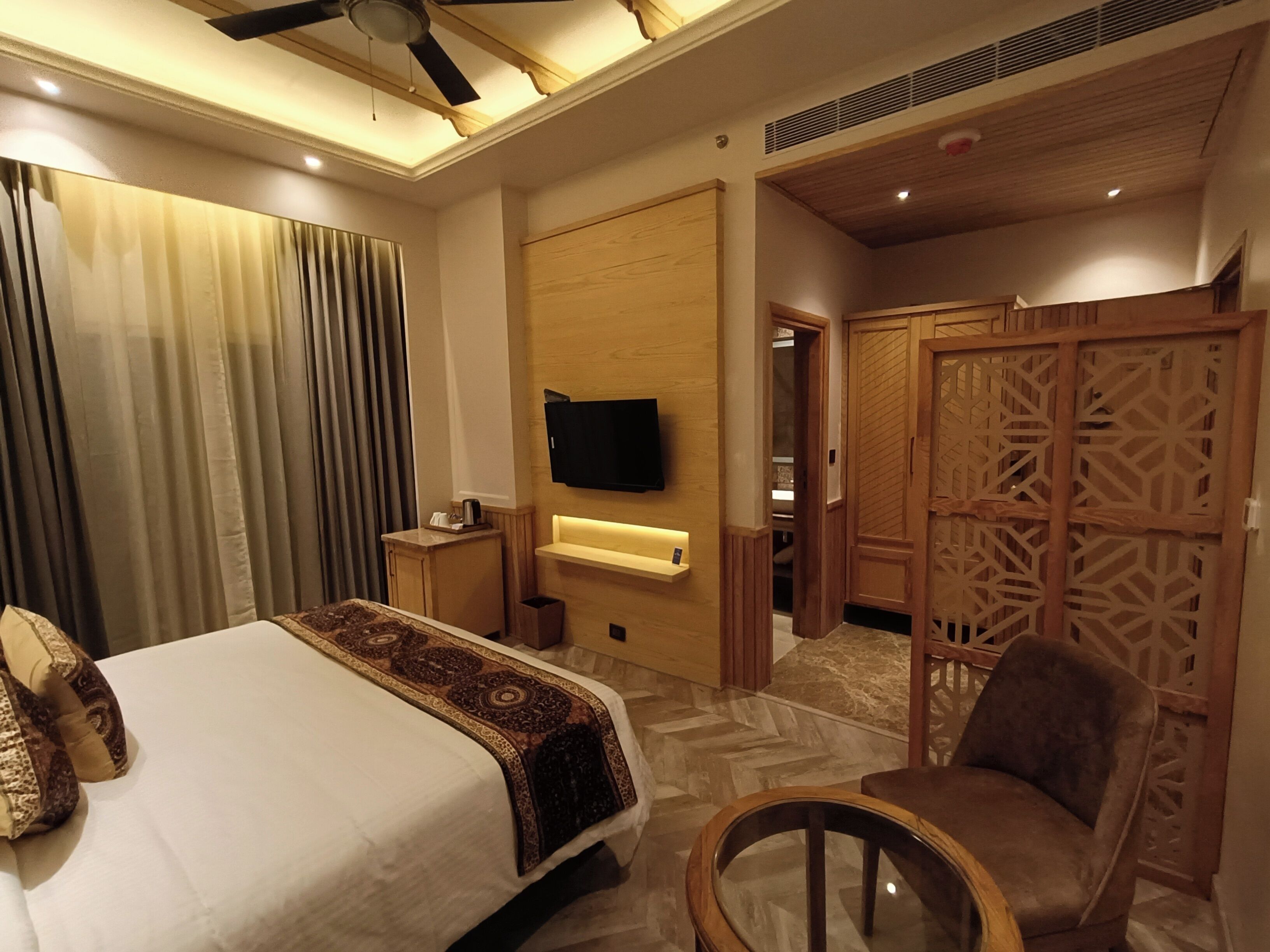 A hotel room with a bed, a chair, a TV mounted on the wall, and a wooden partition.