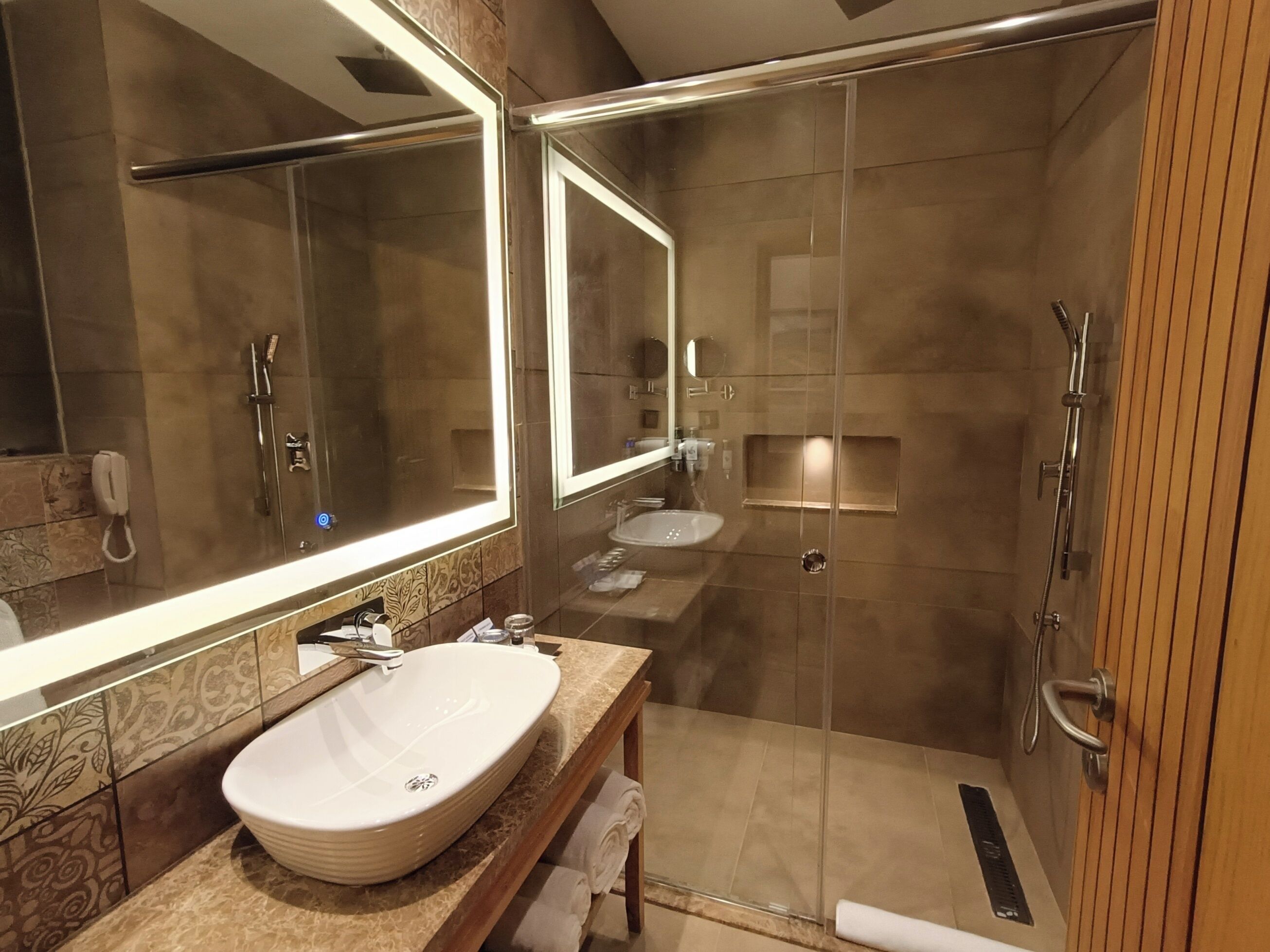 Een moderne badkamer met een grote spiegel, een wastafel en een douche met glazen wanden.