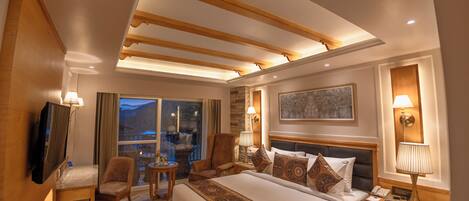 A hotel room with a large bed, a TV, a desk, and a chair. There is a window with a view of the mountains.
