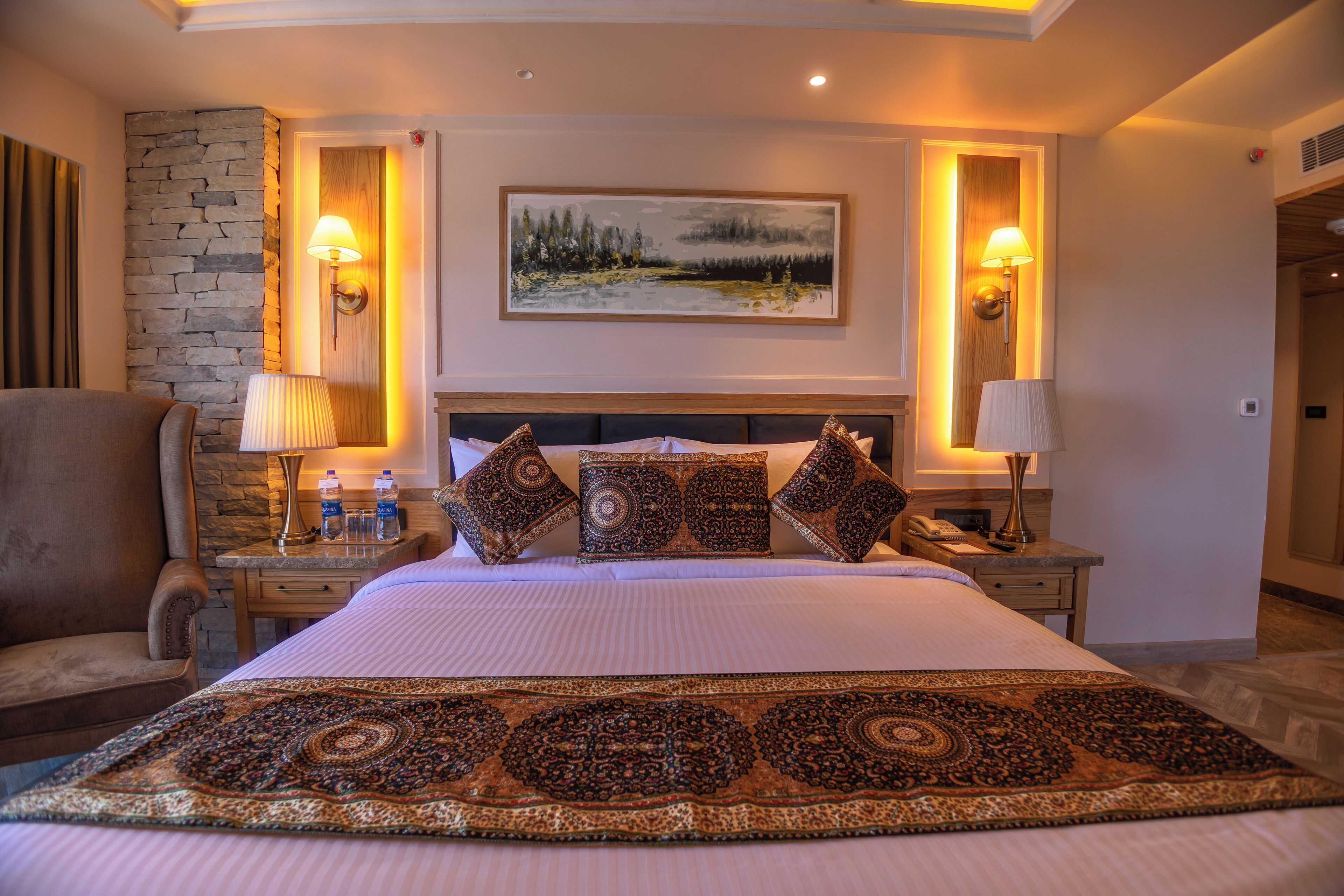 A hotel room with a large bed, a stone accent wall, a painting, and two bedside lamps.