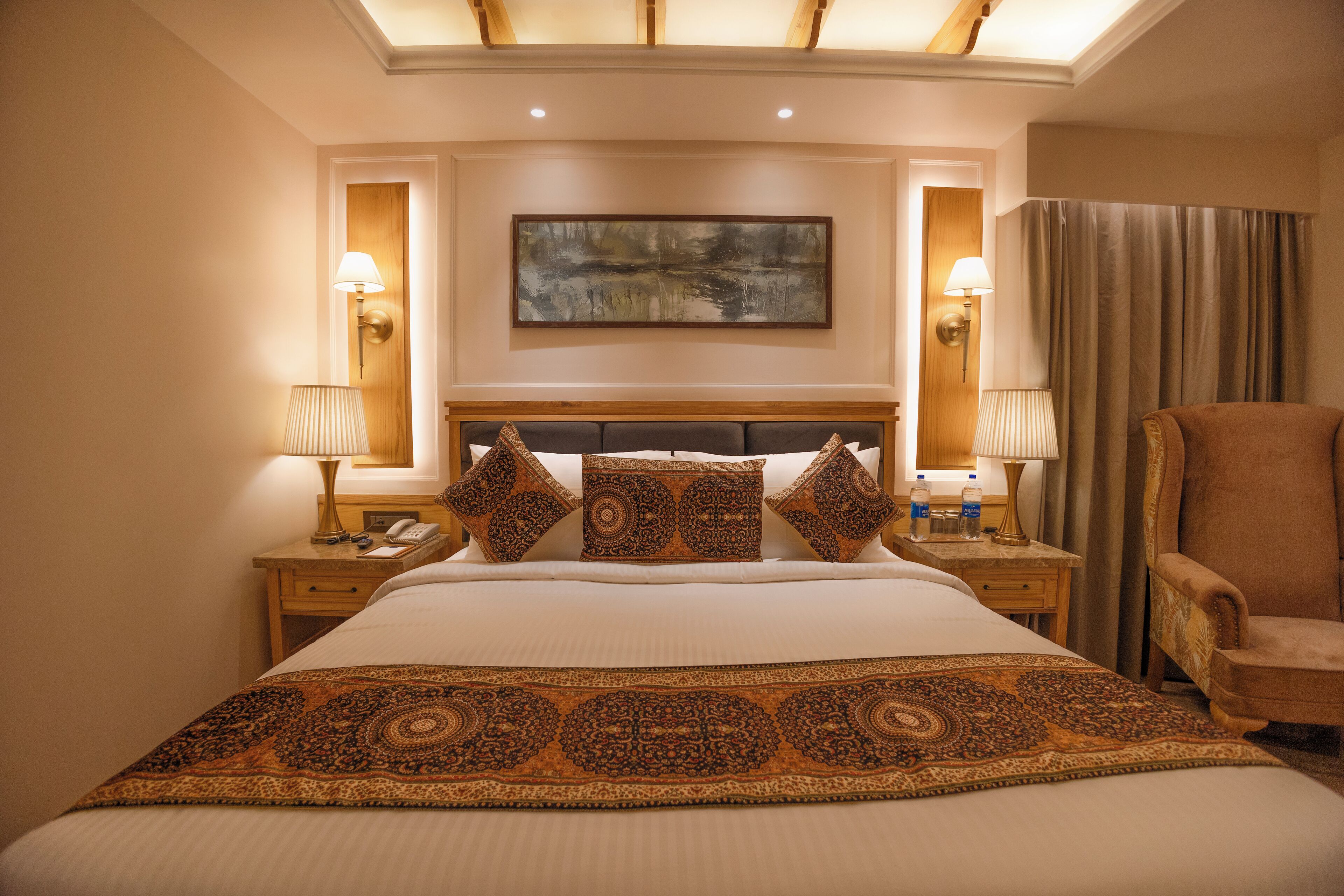 A hotel room with a large bed, two bedside tables, a chair, and a painting on the wall.