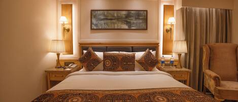 A hotel room with a large bed, two bedside tables, a chair, and a painting on the wall.