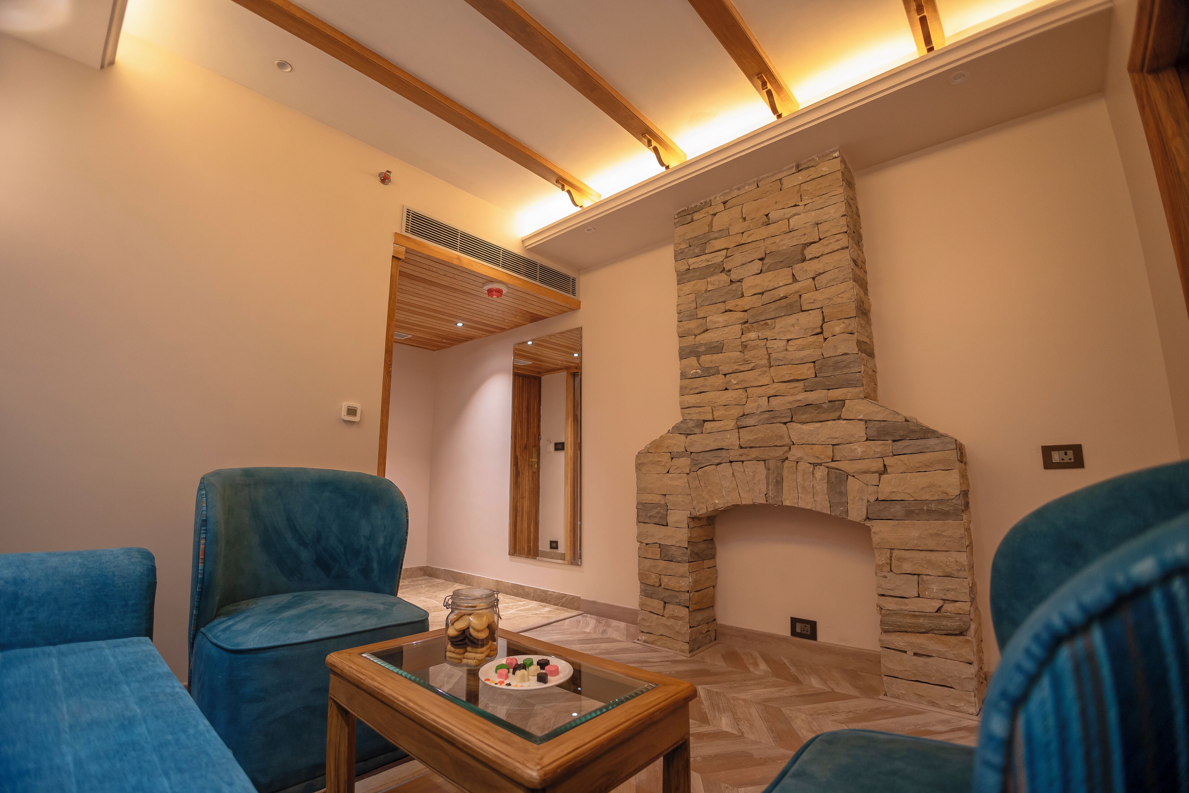 A modern living room with a stone fireplace, blue upholstered chairs, and a glass coffee table with decorative items.
