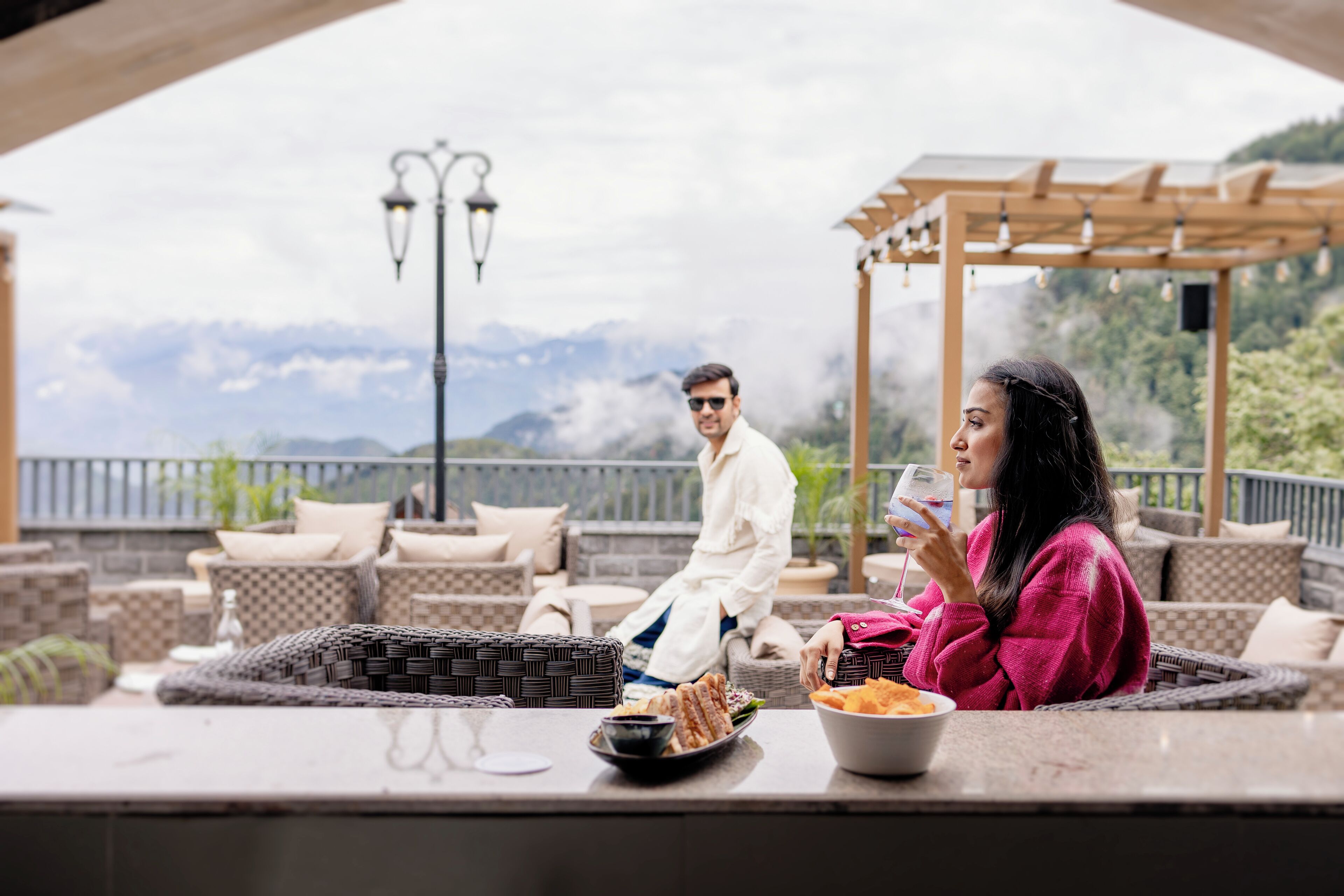 A terrace with wicker furniture, a glass of drink, and a bowl of snacks.
