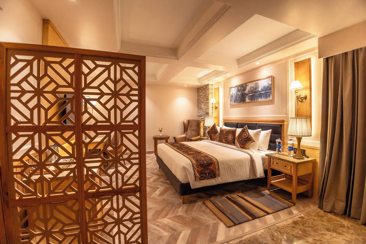 A hotel room with a large bed, a nightstand, a lamp, and a decorative screen.