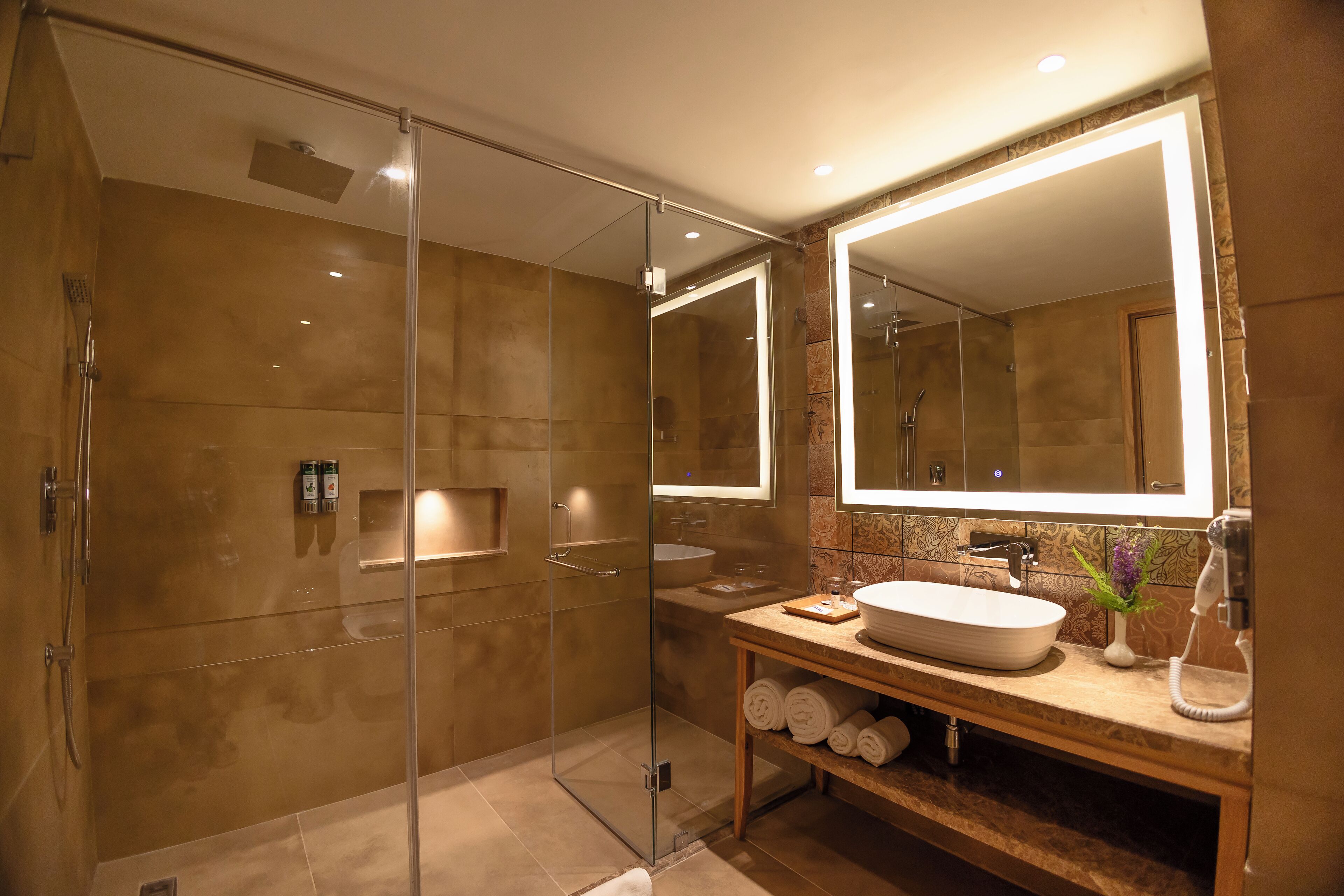 Un baño moderno con ducha de vidrio, un espejo grande y un tocador de madera con lavamanos y perchero.