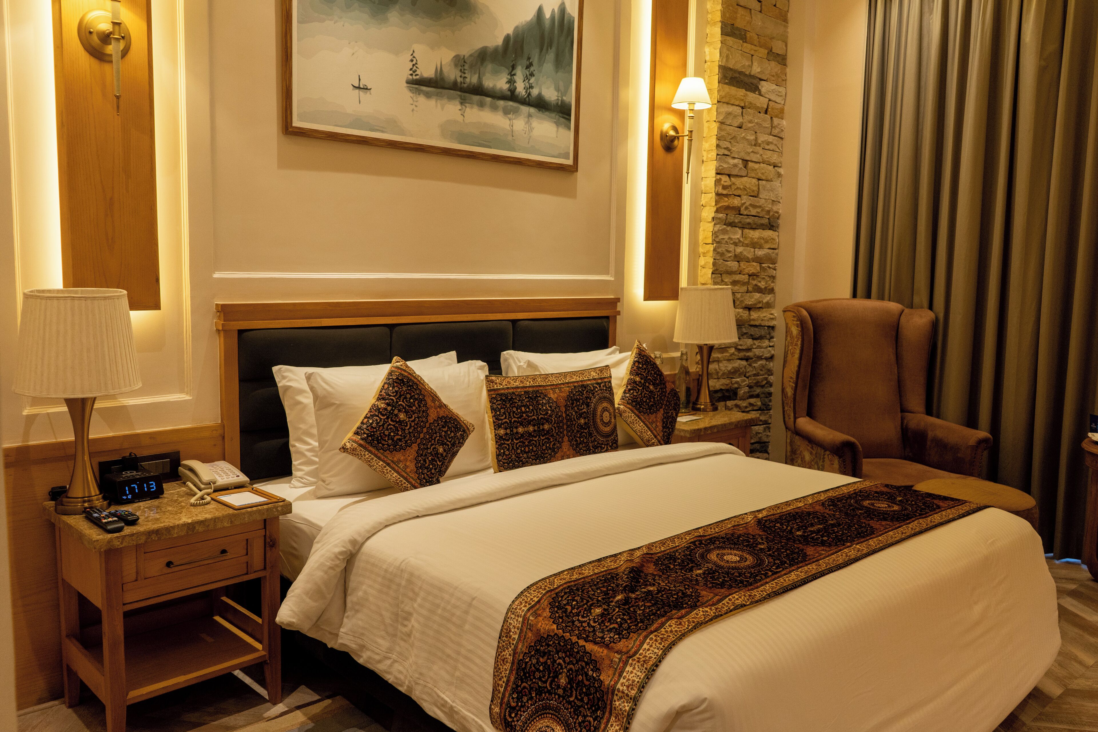 A hotel room with a large bed, two bedside tables, a nightstand, a chair, and a painting on the wall.