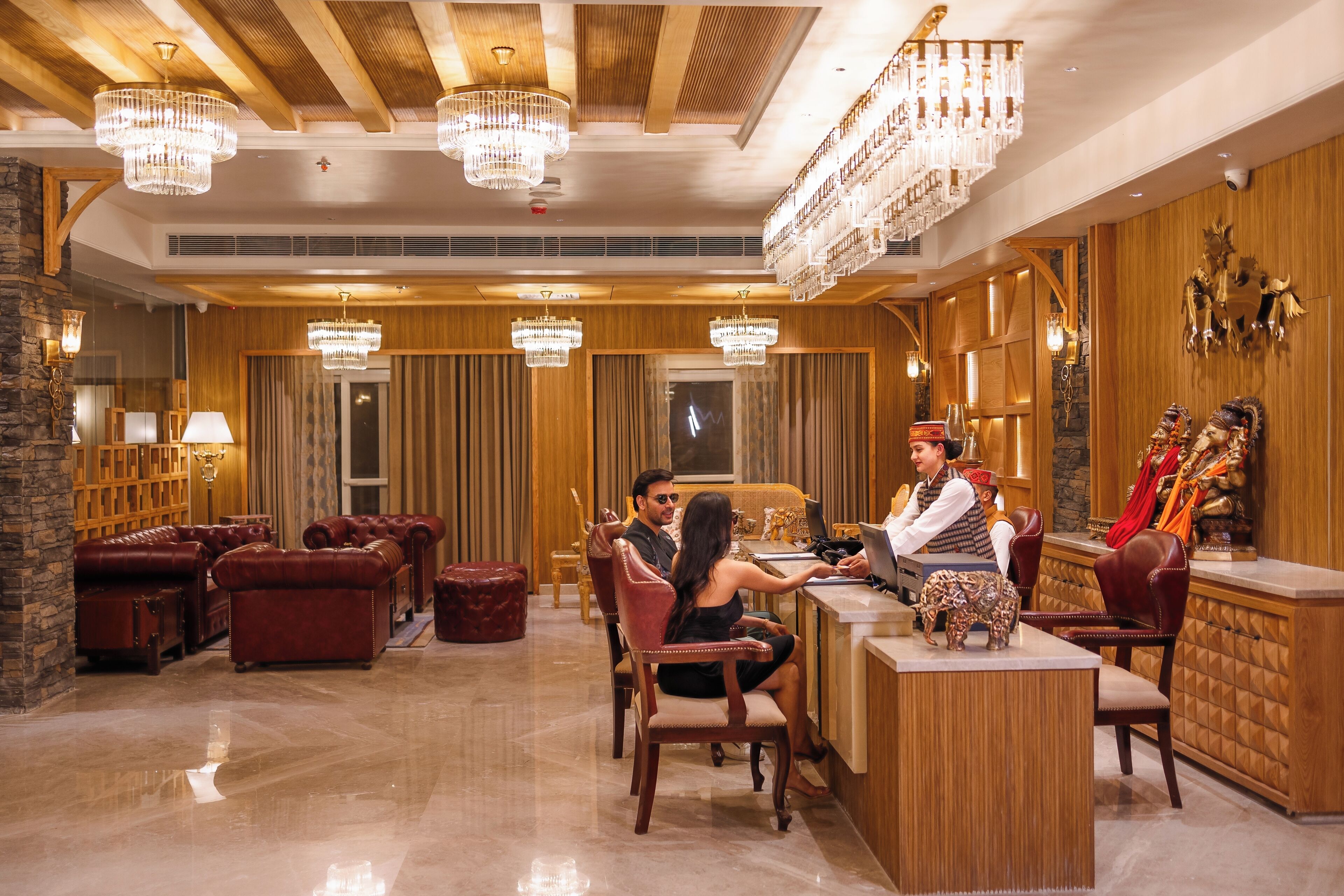 A lobby with leather sofas, wooden paneling, chandeliers, and a reception desk.