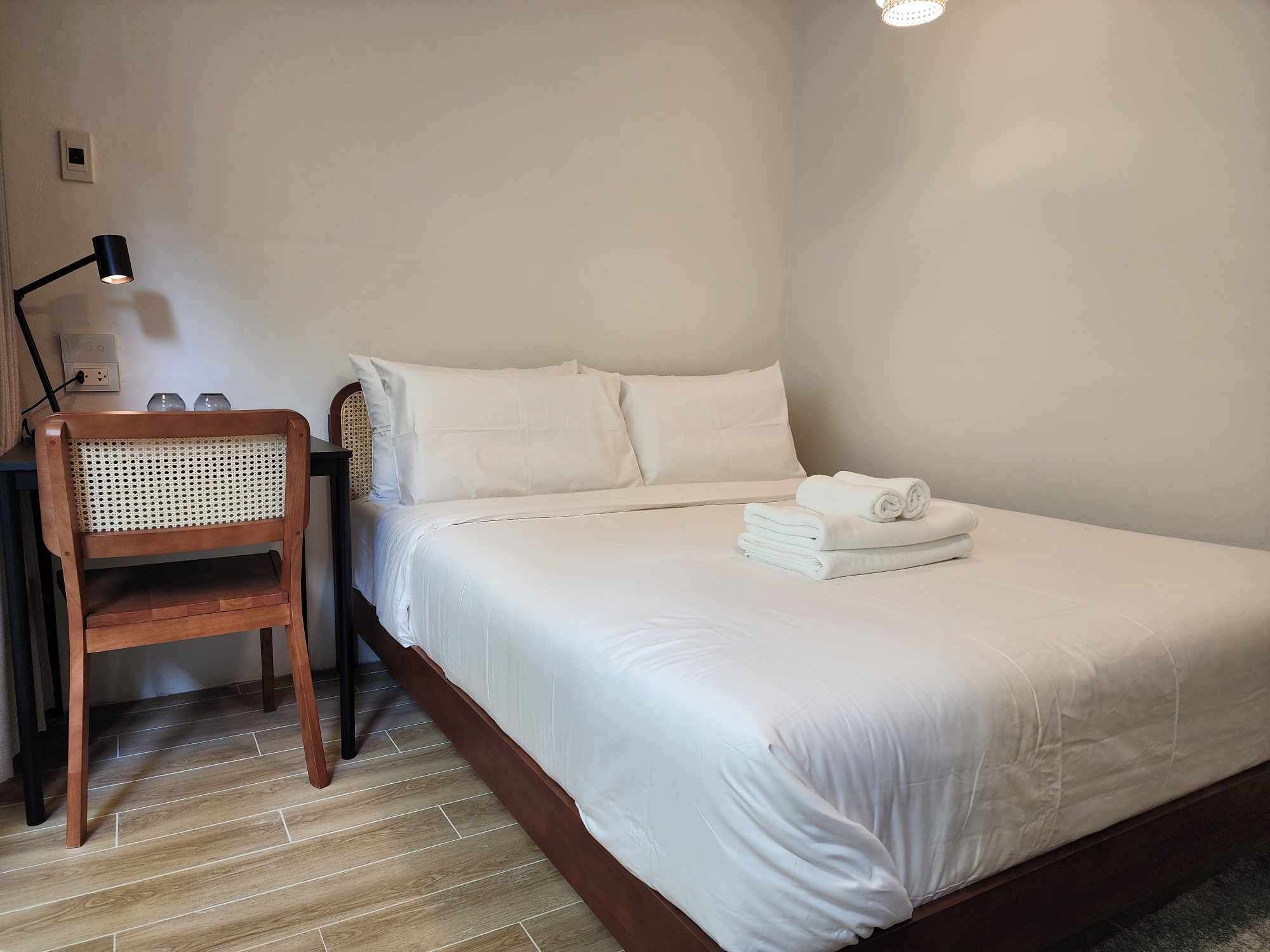 Un lit bien fait, avec du linge de lit blanc et une serviette pliée posée sur le côté.