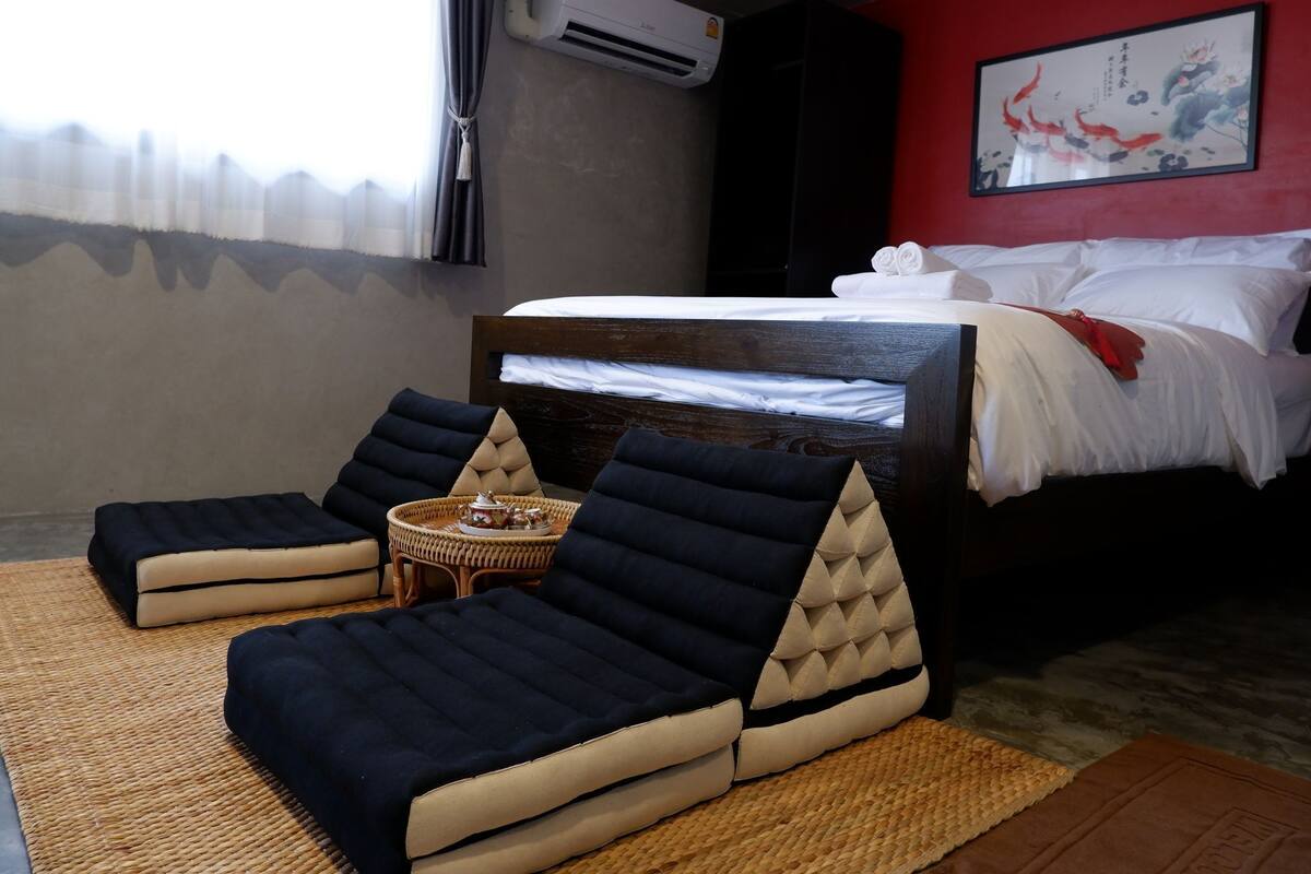 A hotel room with a bed, two lounge chairs, a small table, and a red wall with a painting.