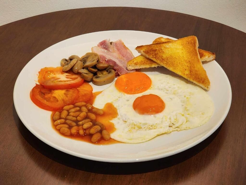 Un plato de comida para el desayuno con huevos, champiñones, tomates, frijoles, tocino y tostadas.