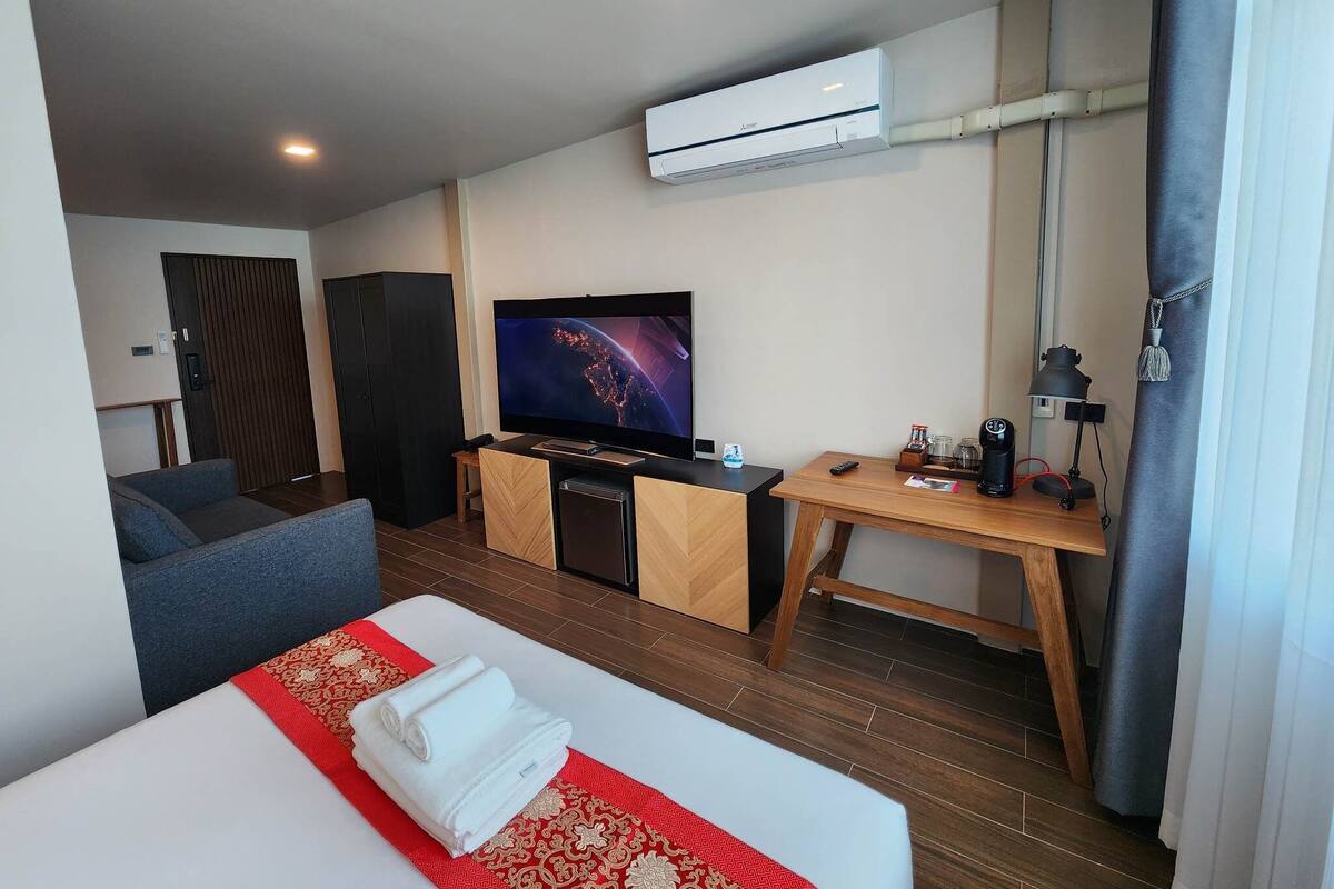 A hotel room with a bed, a TV, a desk, and an air conditioning unit.