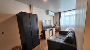 A compact living space with a sofa, a small desk, a TV, and a wardrobe. - Lo-ha Guesthouse Contactless Check-in (Bangkok)