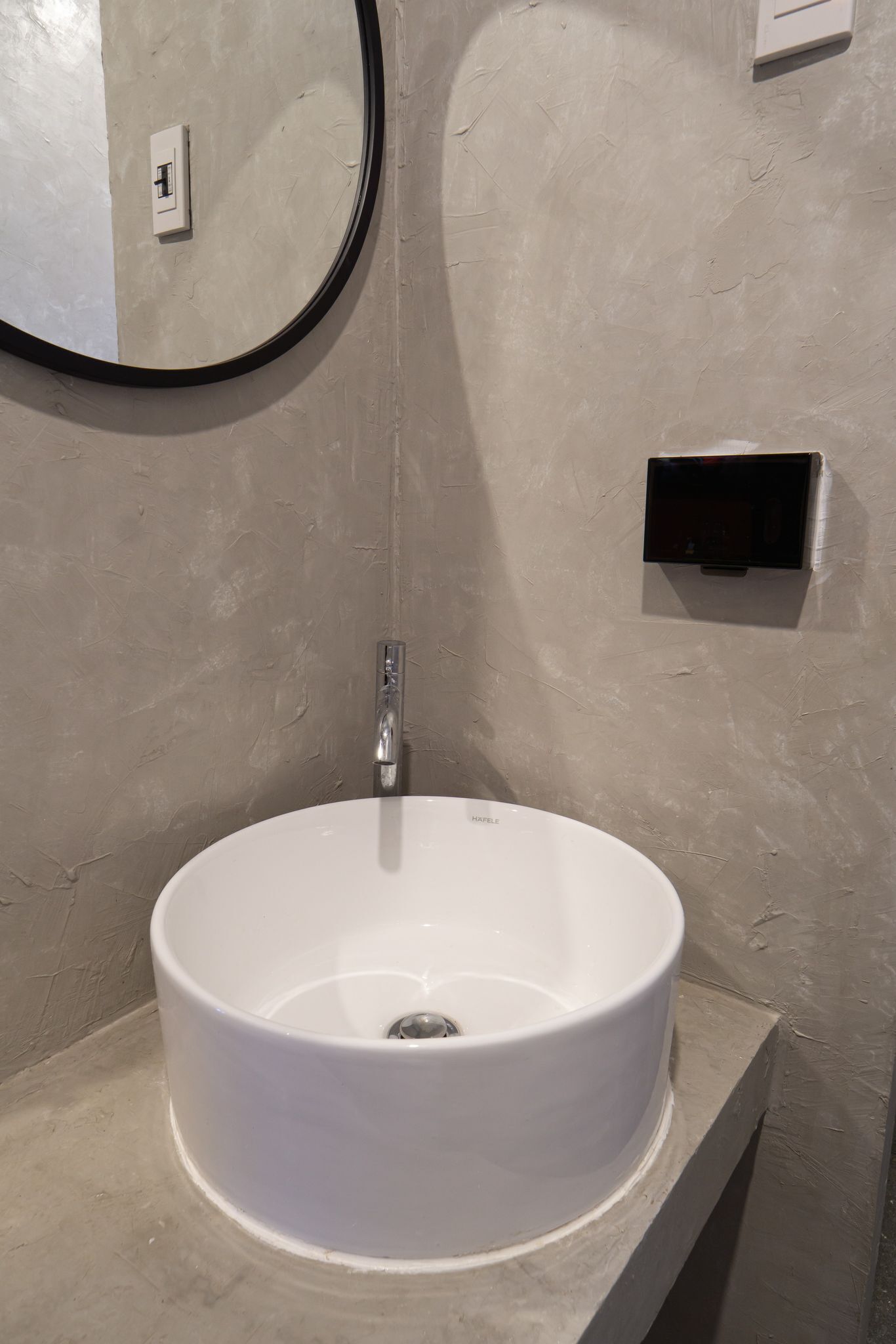 A bathroom with a round white sink, a mirror, and a wall-mounted soap dispenser.