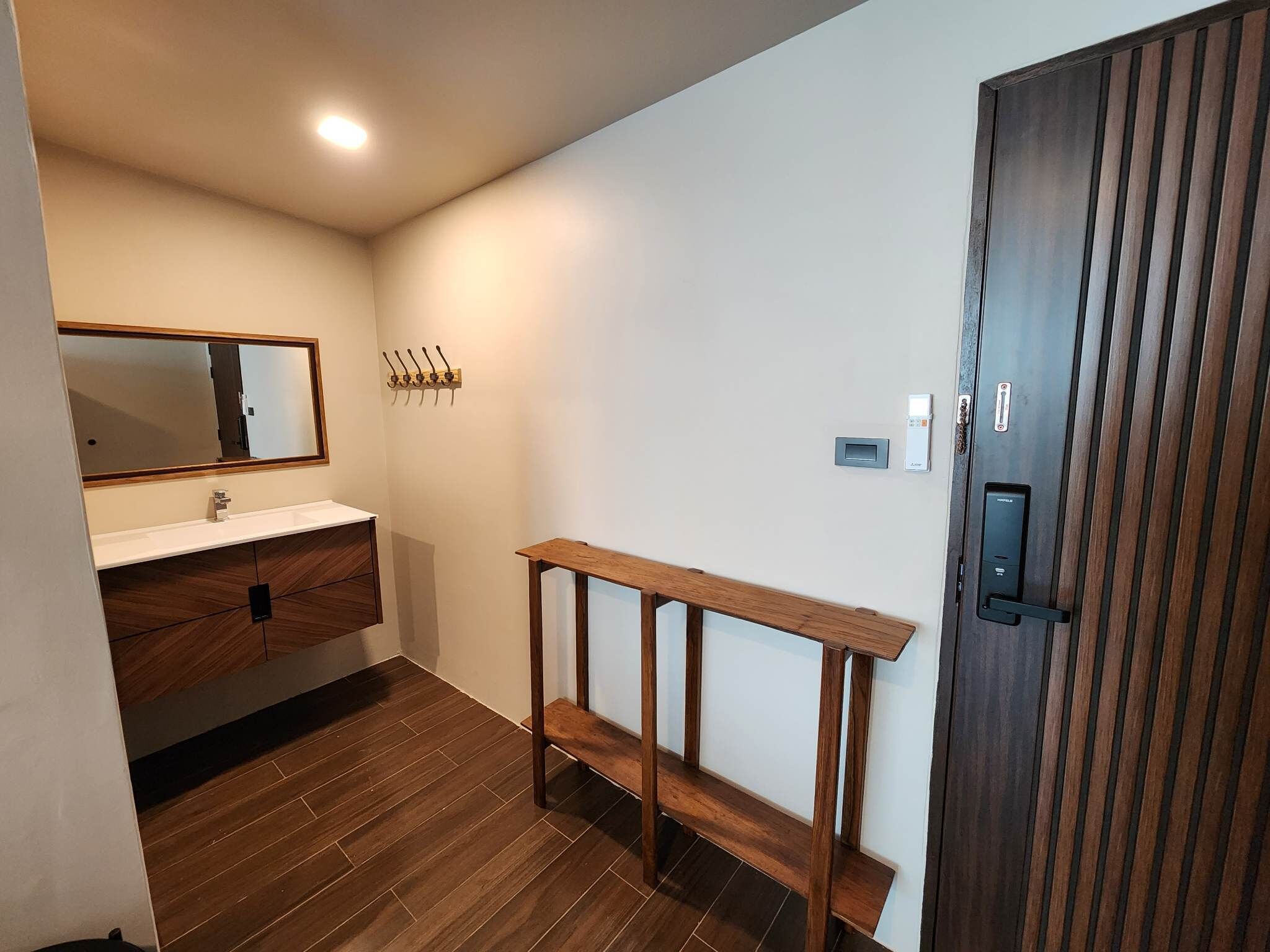 A modern bathroom with a wooden vanity, a mirror, a towel rack, and a wooden bench.
