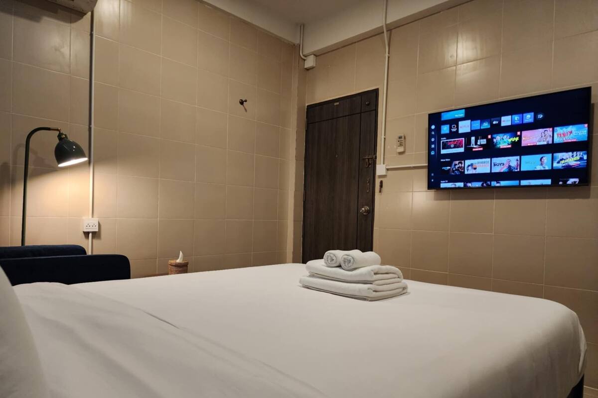 A hotel room with a bed, a TV mounted on the wall displaying various channels, and a dark wooden door.