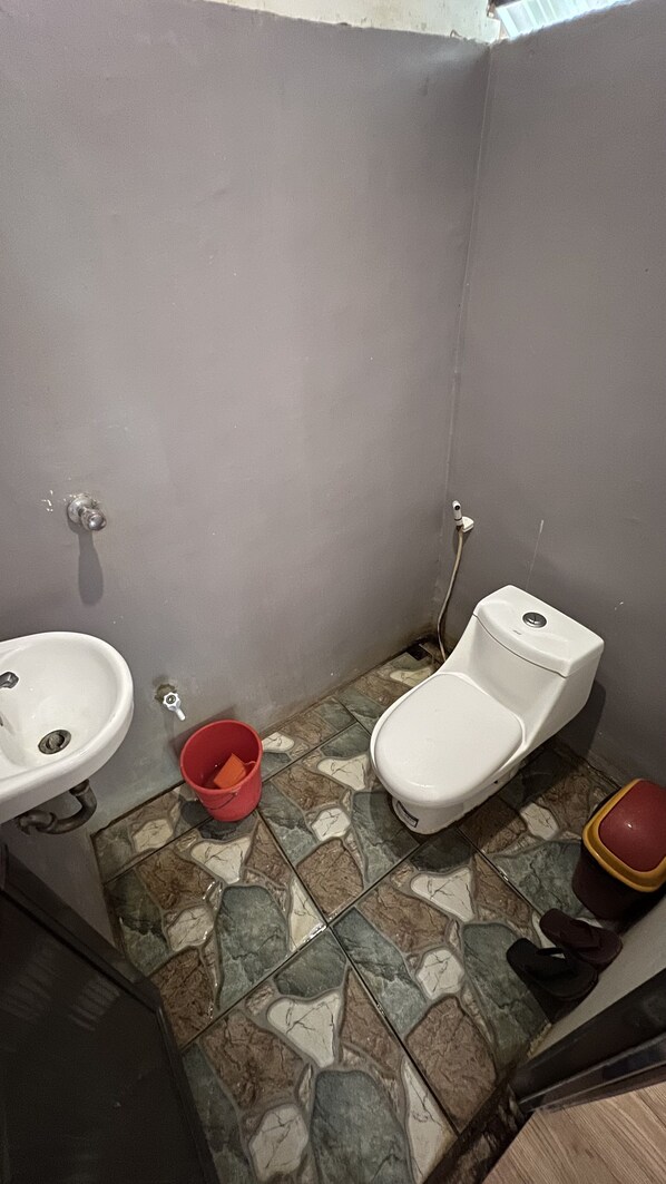 A small bathroom with a sink, toilet, and red bucket. - Banlaw Pool & Garden (Puerto Princesa)