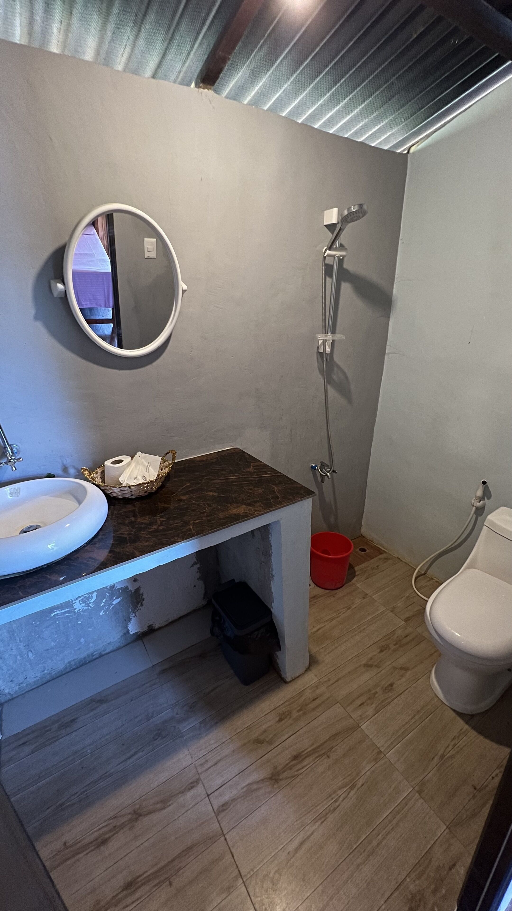 A bathroom with a round mirror, a sink, a shower, and a toilet.