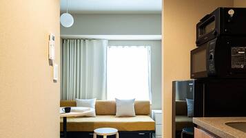 Une chambre d’hôtel compacte comprenant un coin cuisine, un canapé-lit, une petite table et une fenêtre avec des rideaux.