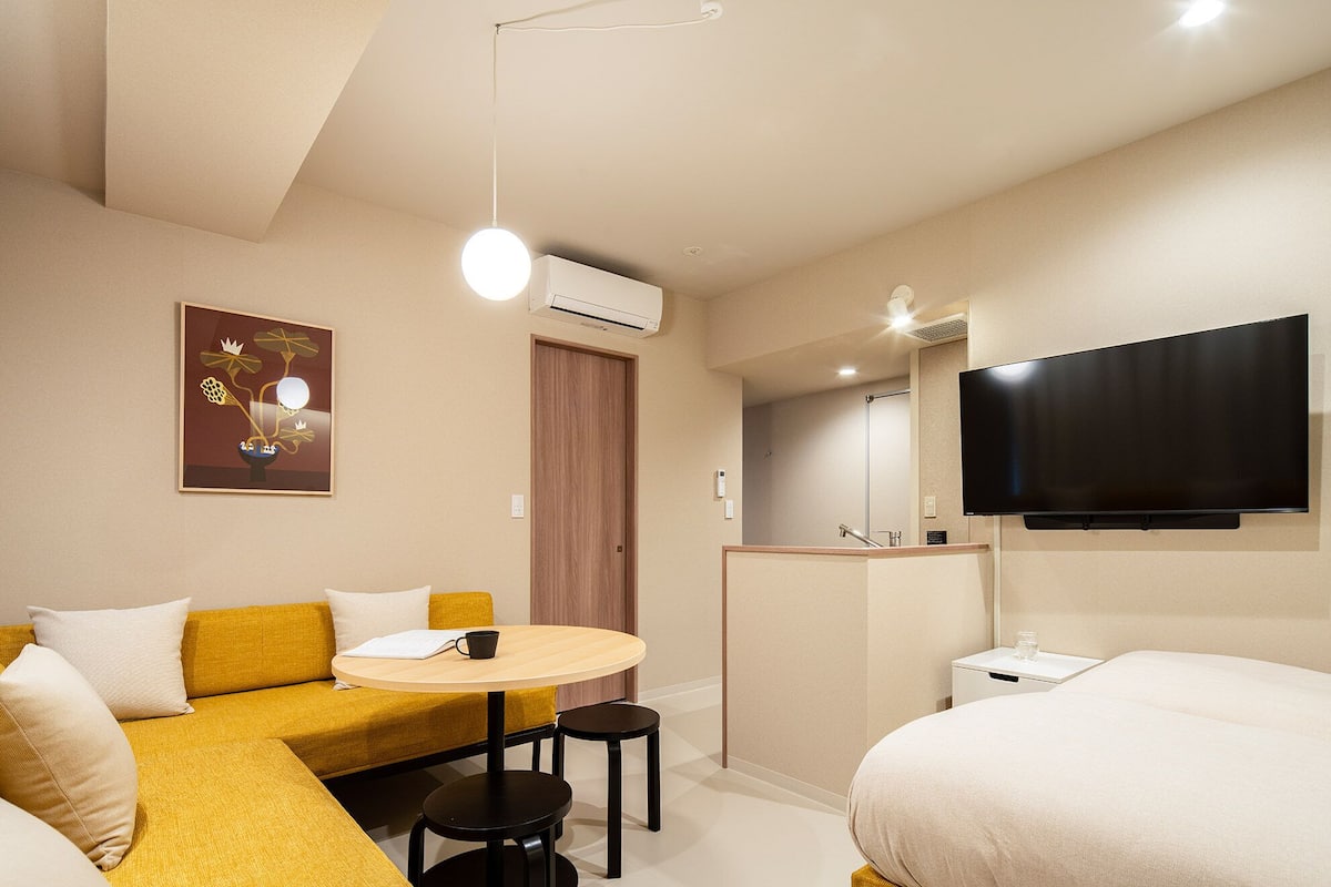 A hotel room with a sofa, a round table, a bed, a TV, and an air conditioning unit.