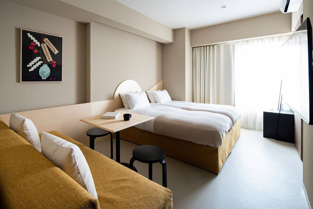 A hotel room with two beds, a small table, and a sofa.