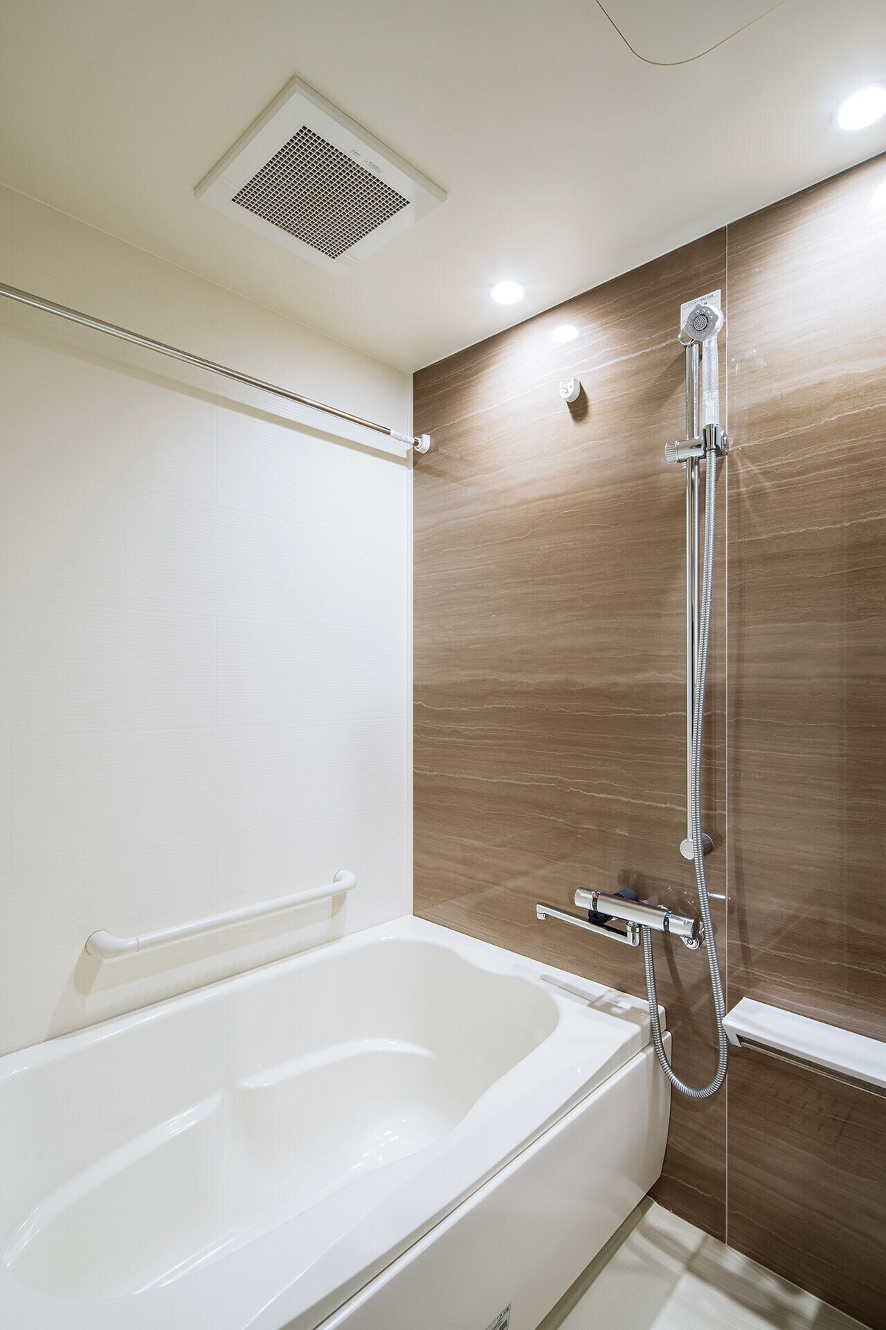 Une salle de bain moderne avec une baignoire blanche, une douche équipée d’un pommeau de douche à main et un panneau de commande fixé au mur.