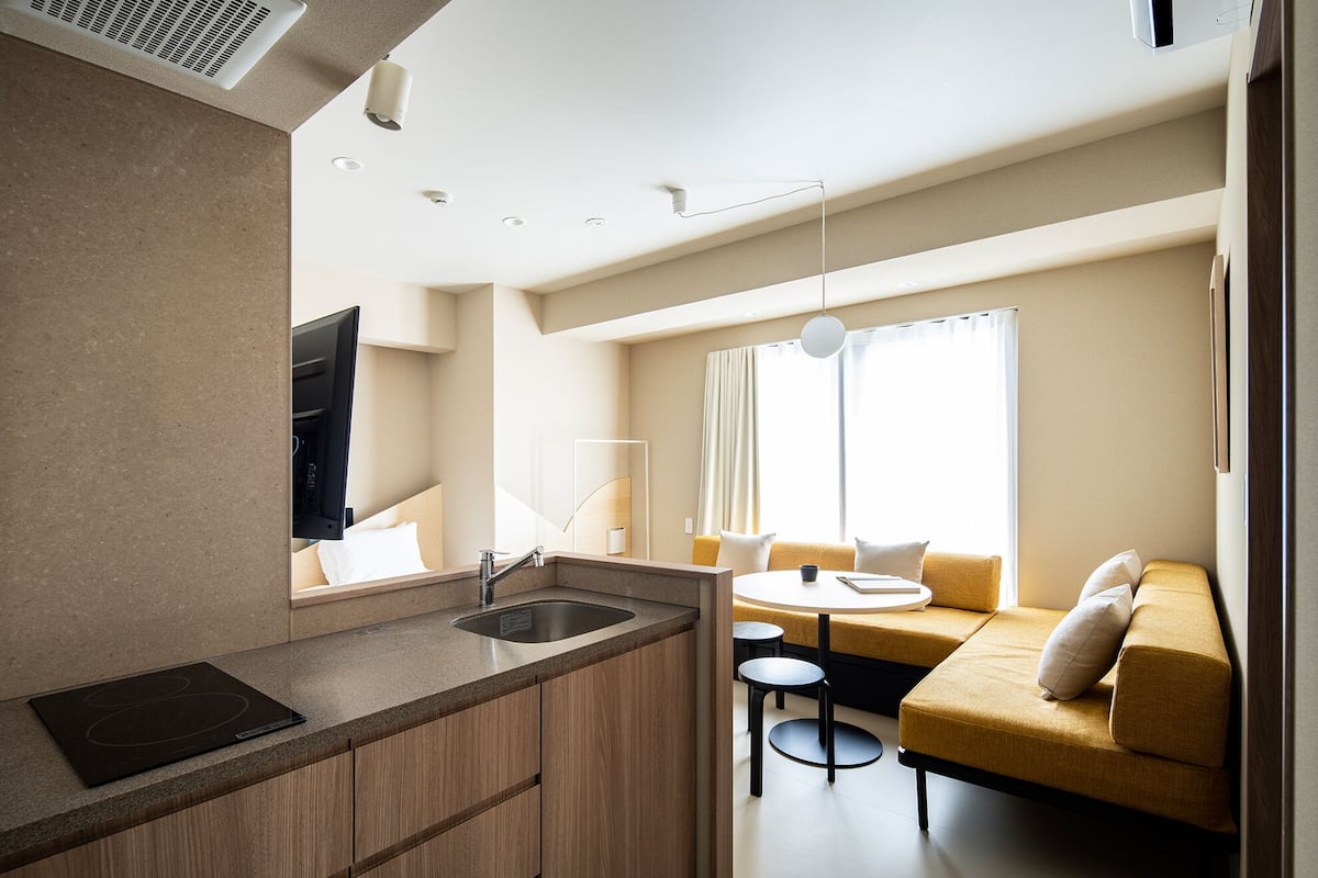A modern hotel room with a kitchen area, a sofa, and a dining table.