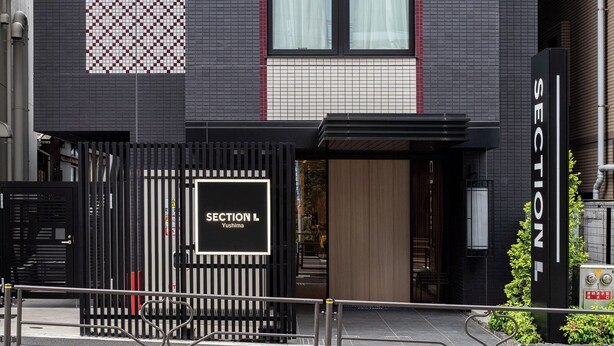 A modern building with a black facade, a gated entrance, and a sign reading "SECTION L Yushima". - Section L Yushima - Ueno (Tokyo)