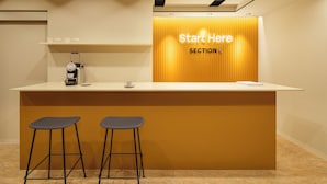 A reception area with a counter, two bar stools, a coffee machine, and a sign that reads 'Start Here SECTION L'. - Section L Yushima - Ueno (Tokyo)