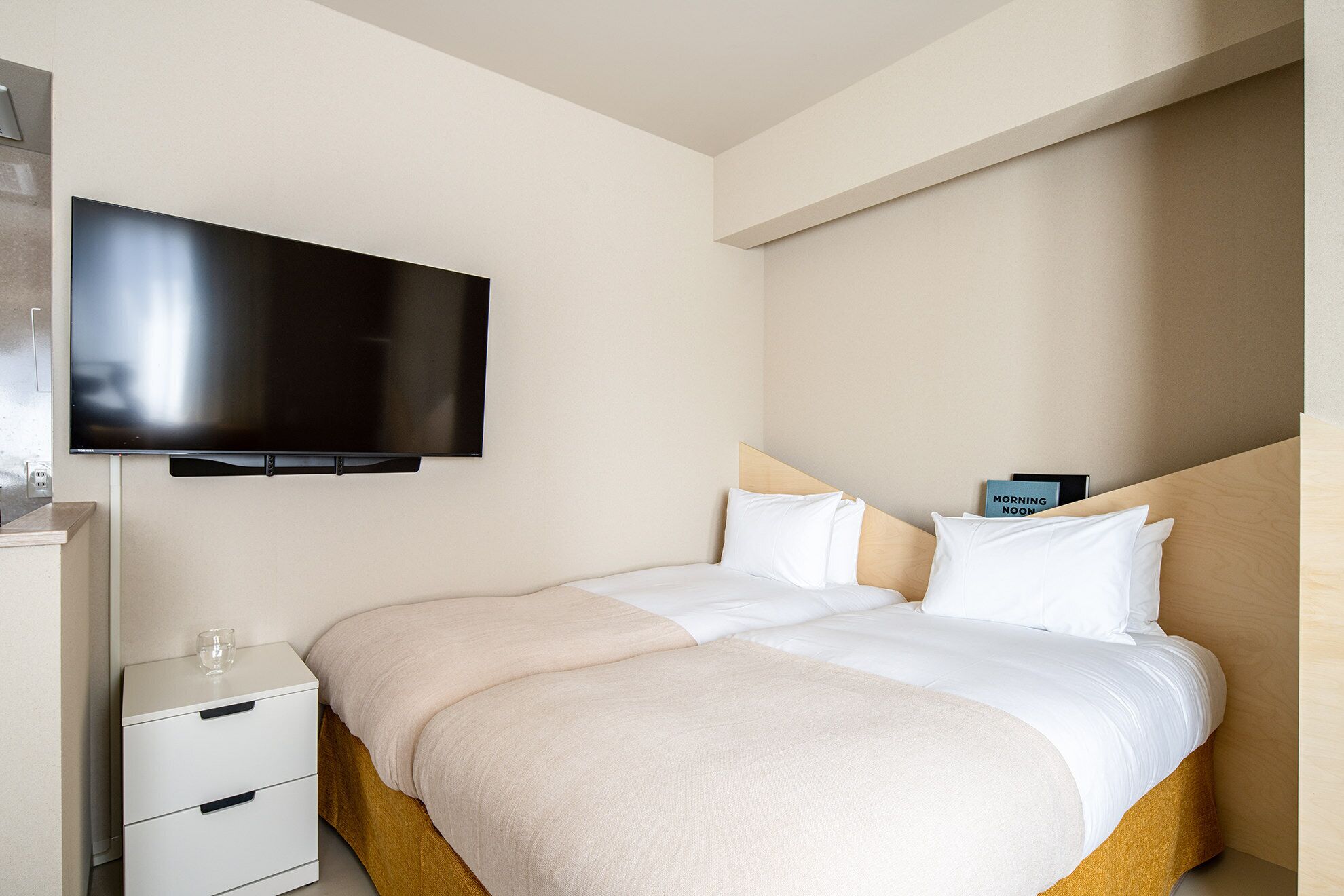 A hotel room with a bed, a bedside table, a TV, and a nightstand.