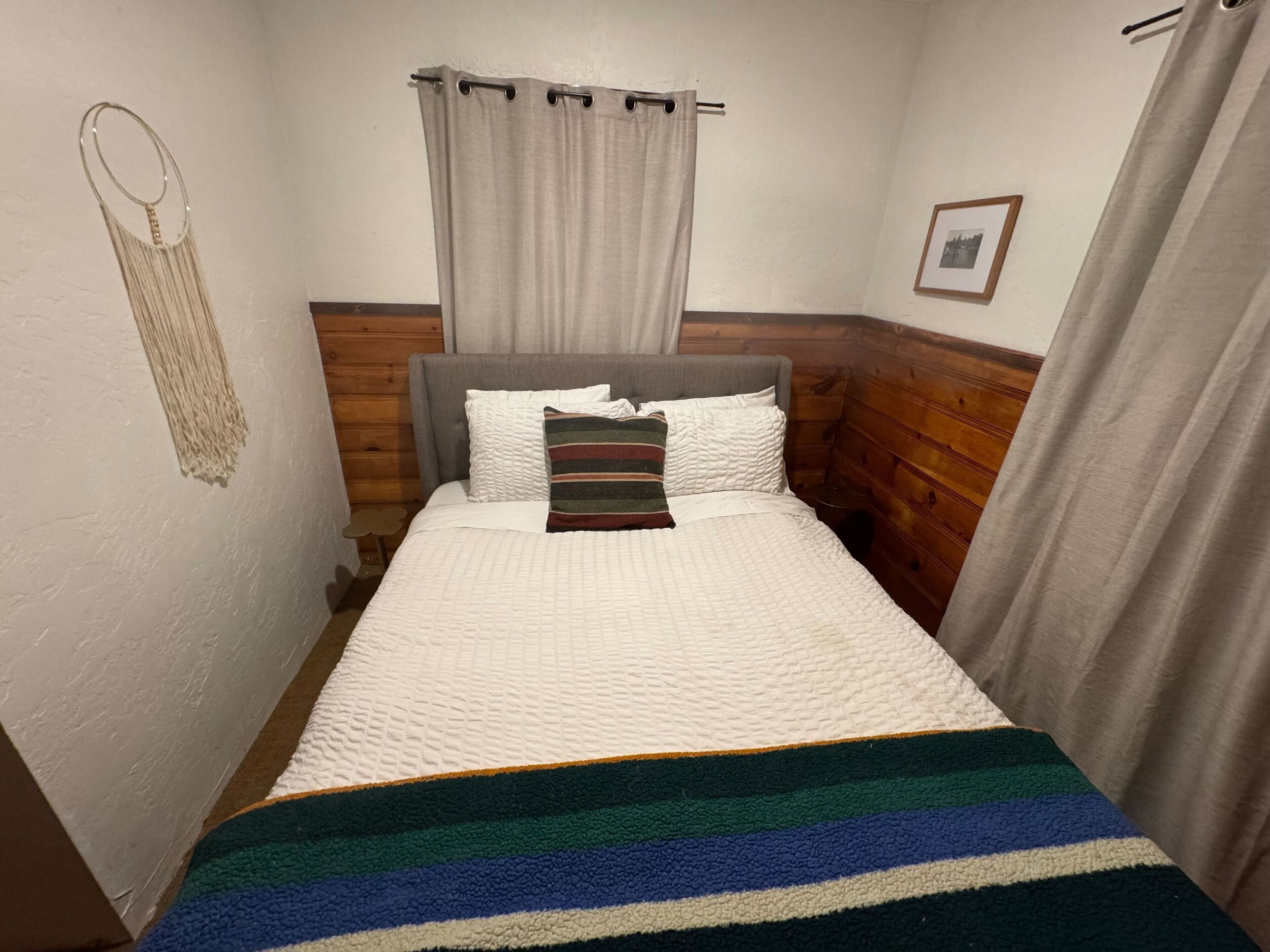 A small, cozy room with a single bed, a wooden headboard, a bedside table, and a wall-mounted hook.