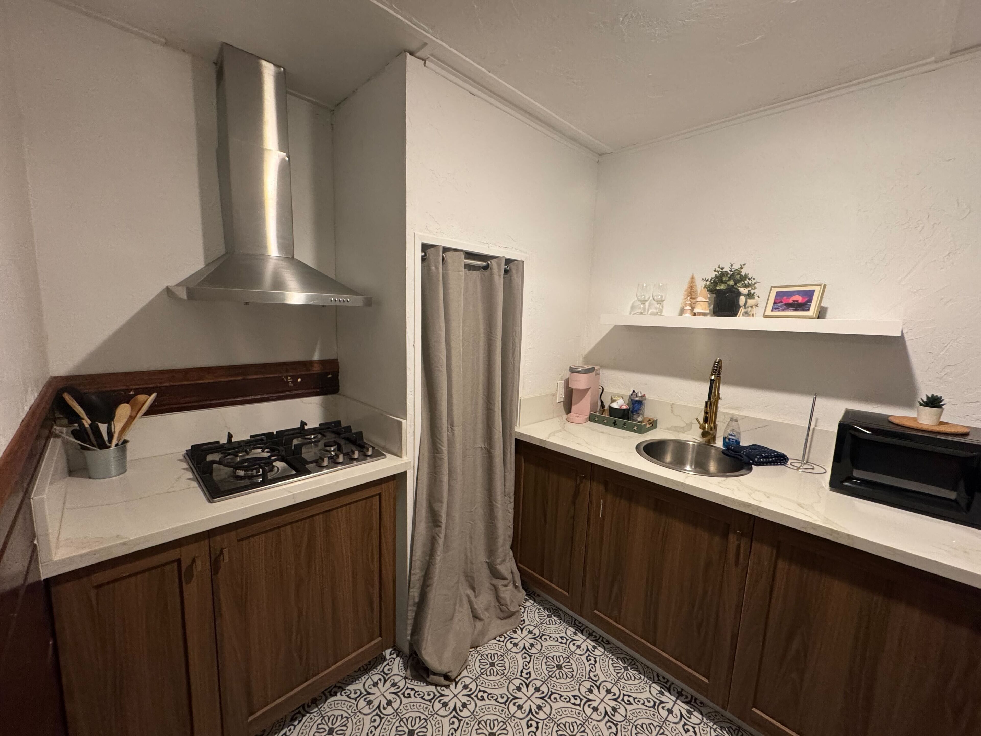 A compact kitchen with a gas stove, stainless steel sink, and a built-in range hood.