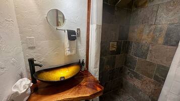 A bathroom with a wooden vanity, a round mirror, a sink, and a shower area with stone tiles.