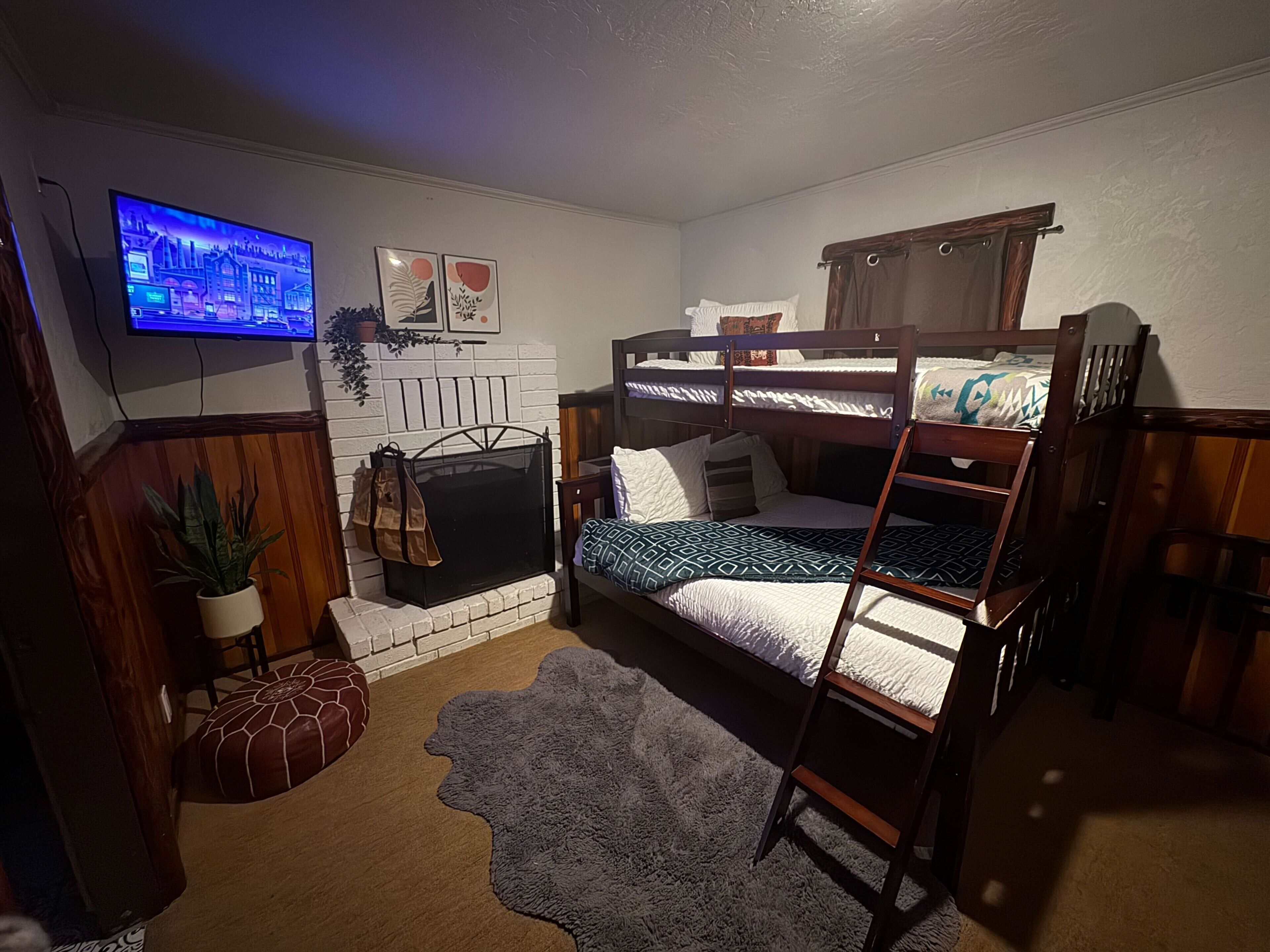 A cozy bedroom with bunk beds, a fireplace, a TV, and a rug.