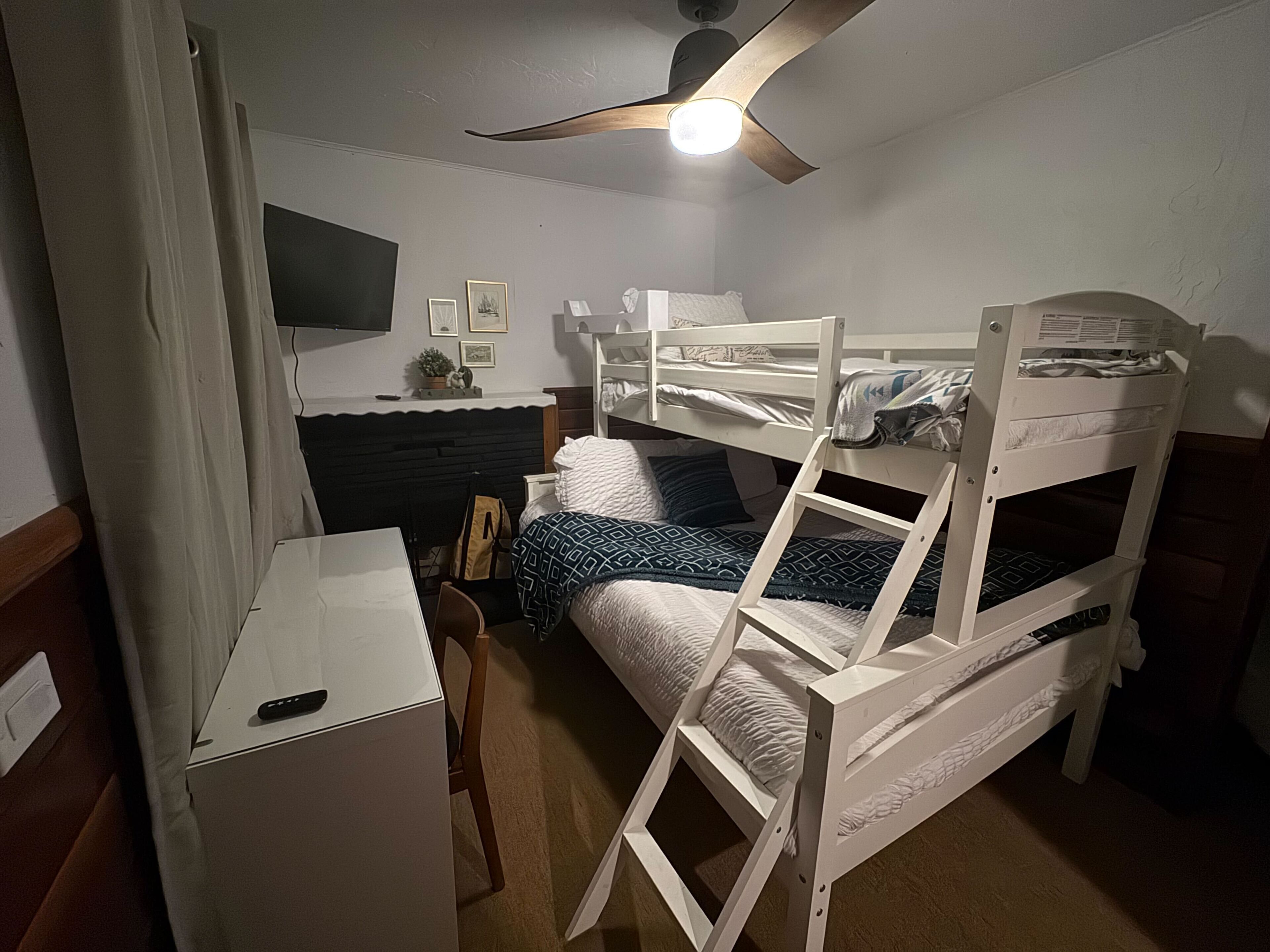A bunk bed room with a desk, chair, and a ceiling fan.