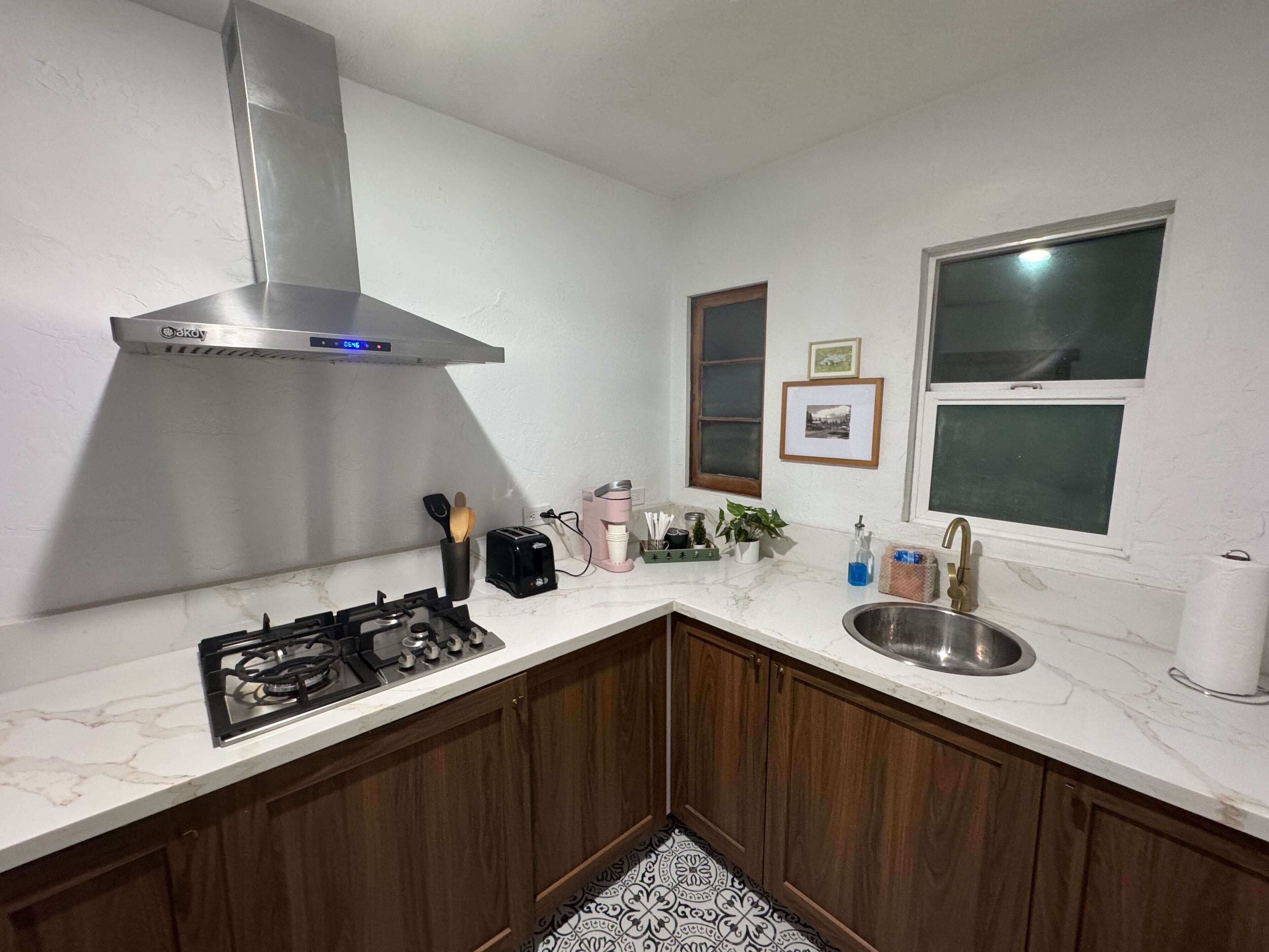 A compact kitchen with a gas stove, stainless steel sink, and a modern range hood.