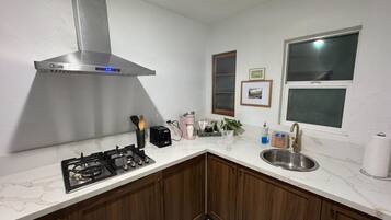 A compact kitchen with a gas stove, stainless steel sink, and a modern range hood.