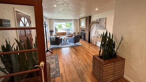 Un vaste espace de vie doté d’un plancher en bois, d’un ensemble de canapés, d’une cheminée et d’une grande plante en pot.
